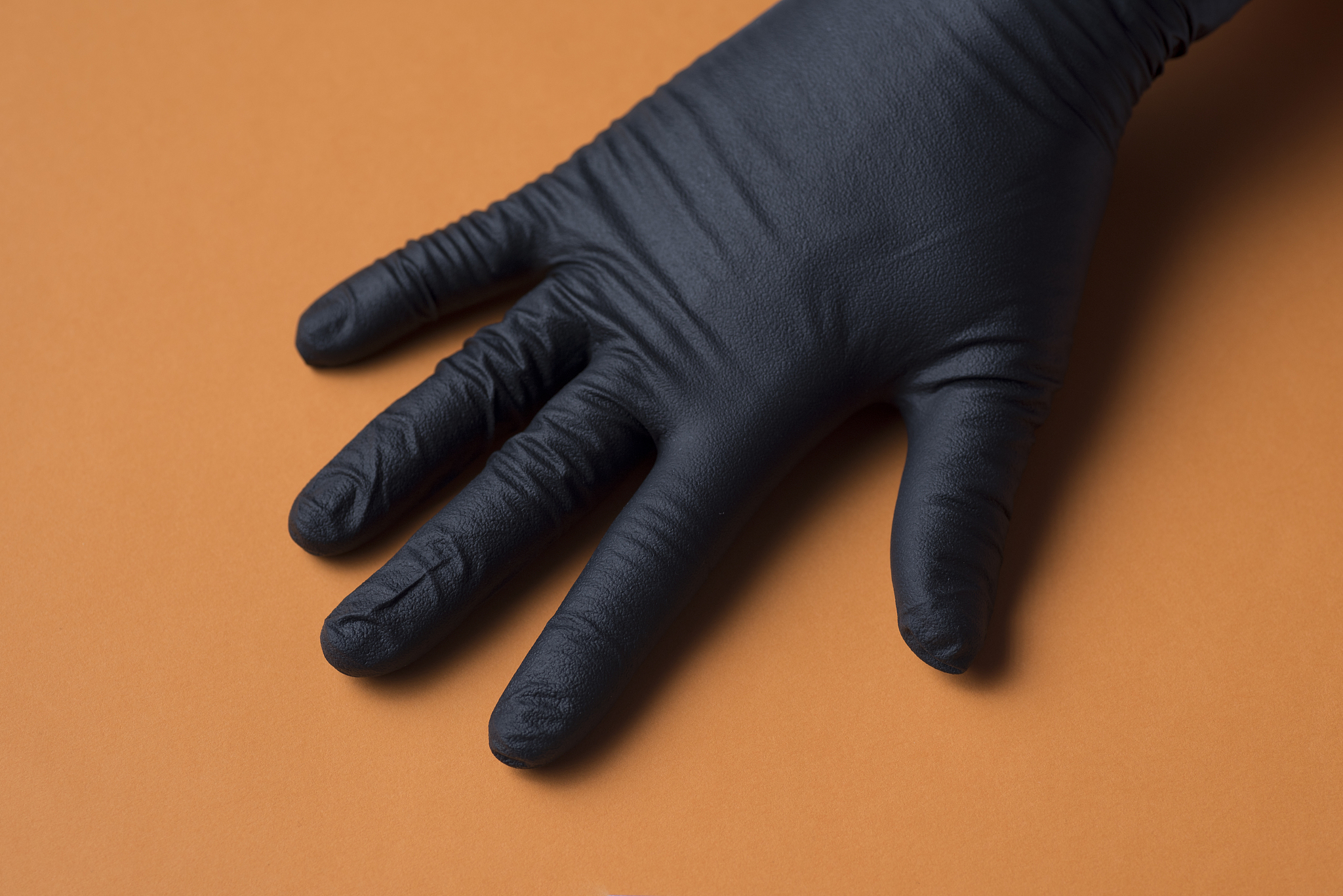 black sanitary glove placed on a hand, on orange background