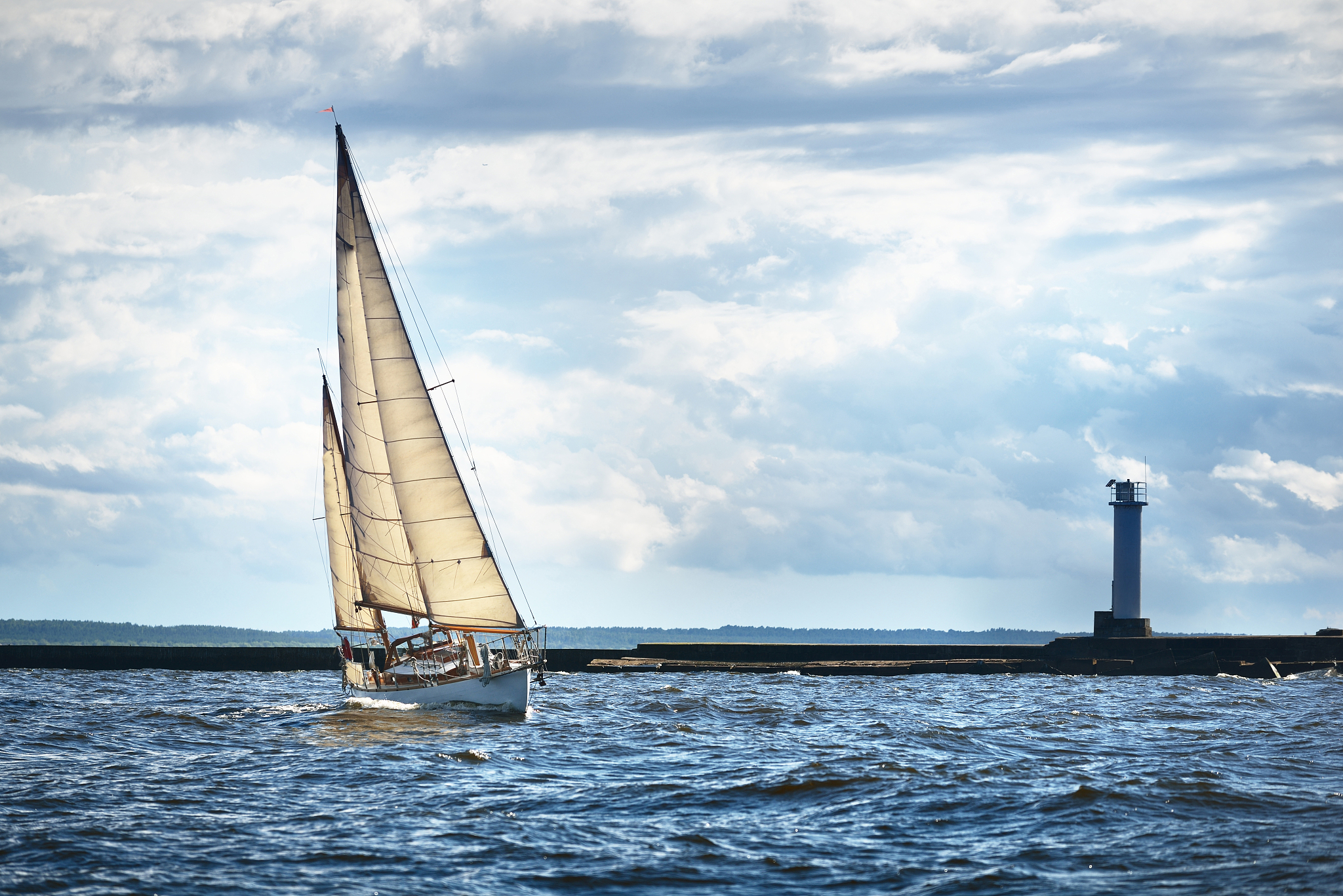 vintage white wooden sailing boat sails on a cloudy day. lightho