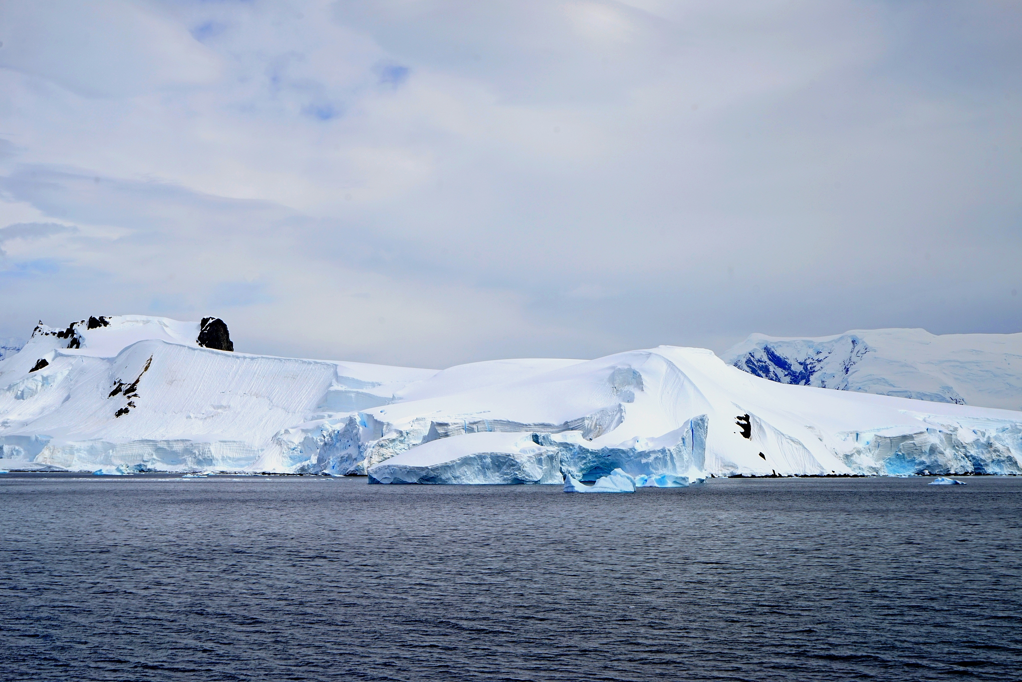 iceberg behind the deep blue sea. white clouds make the iceberg 