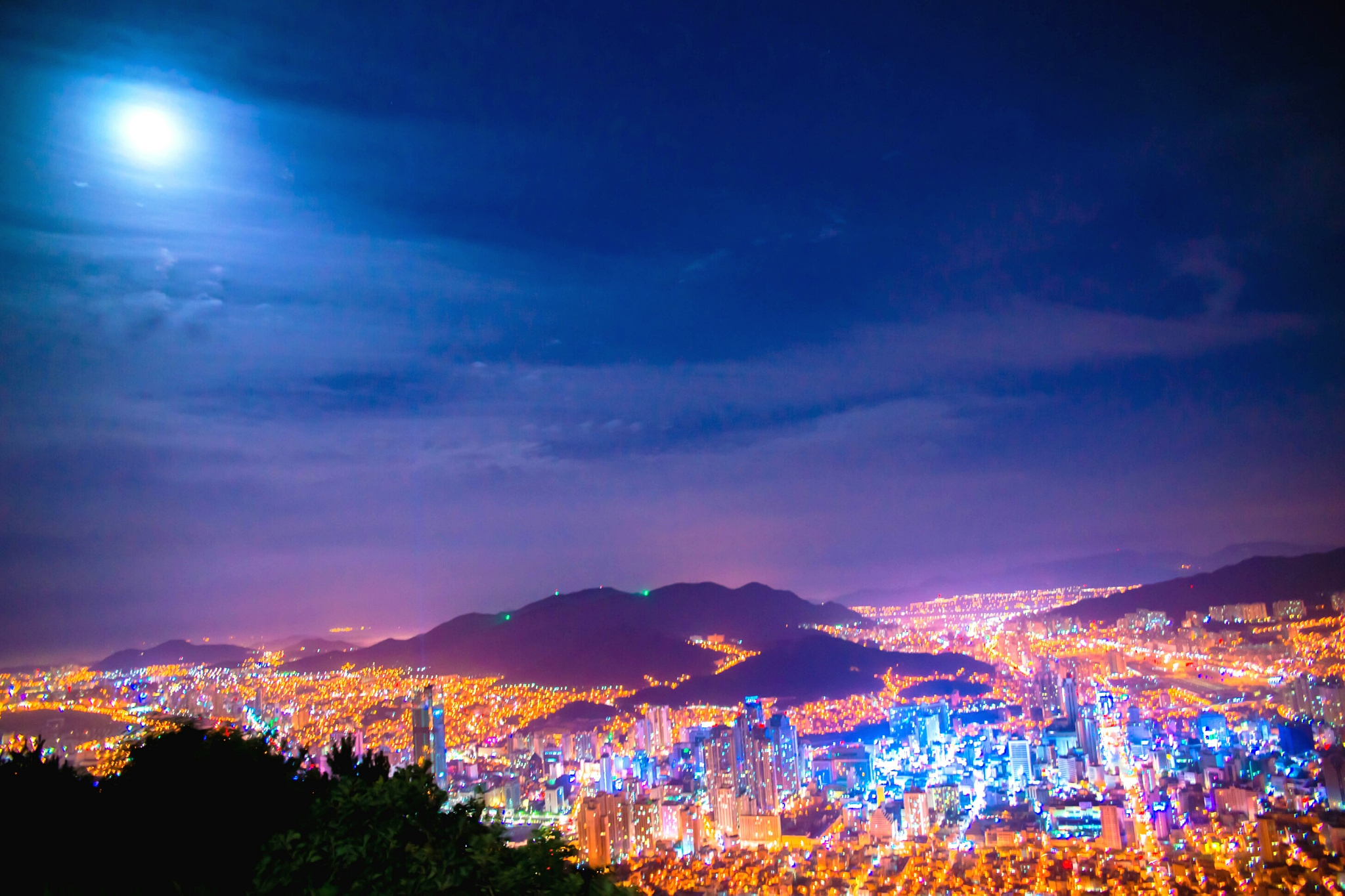 illuminated city and mountains against blue sky