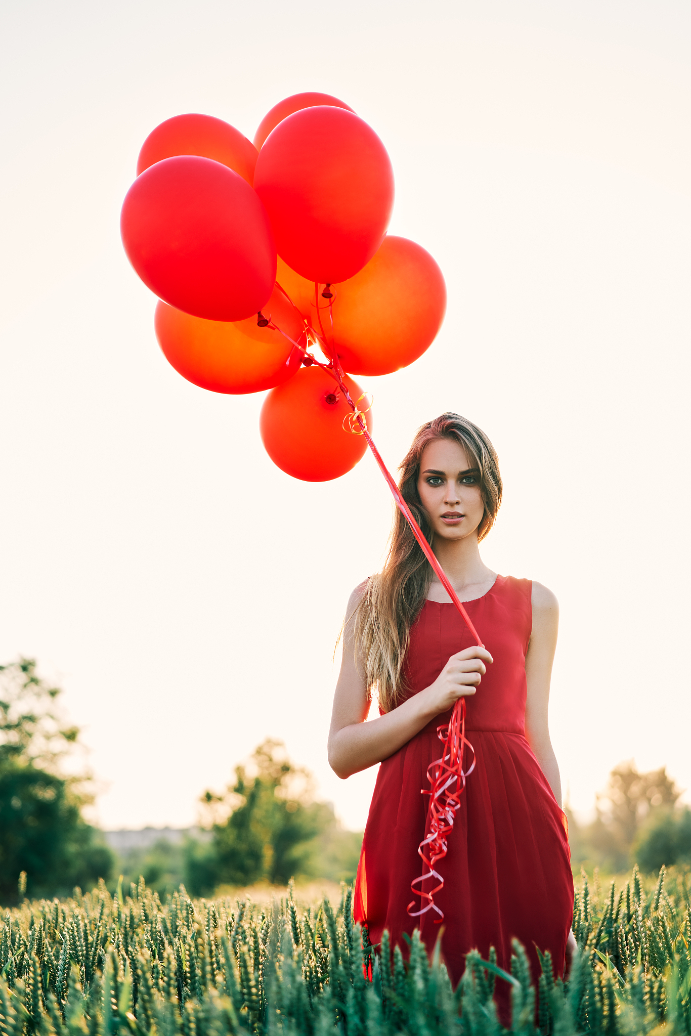 young beautiful woman in red dress posing in green field with re