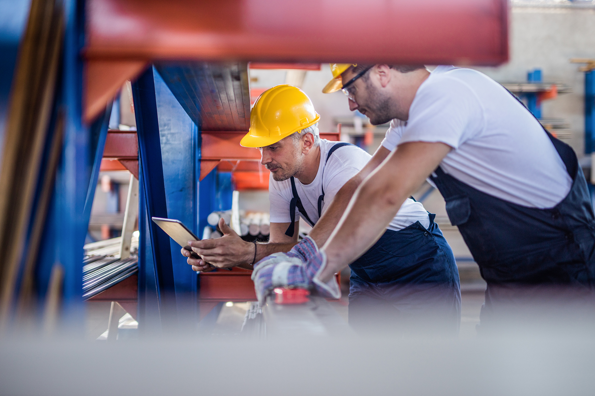 two metal workers cooperating while using touchpad in a factory.