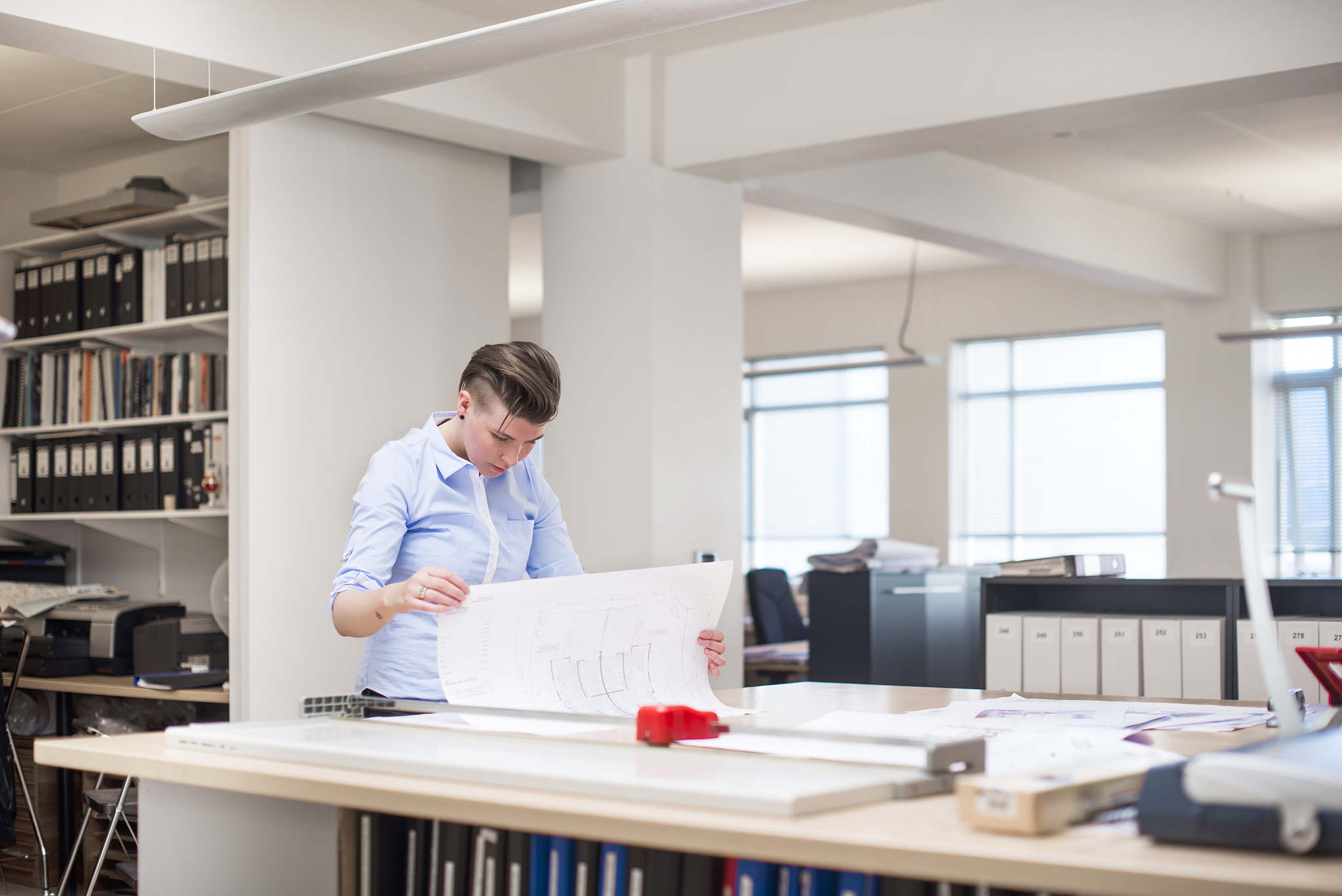 female professional examining blueprint at desk in office