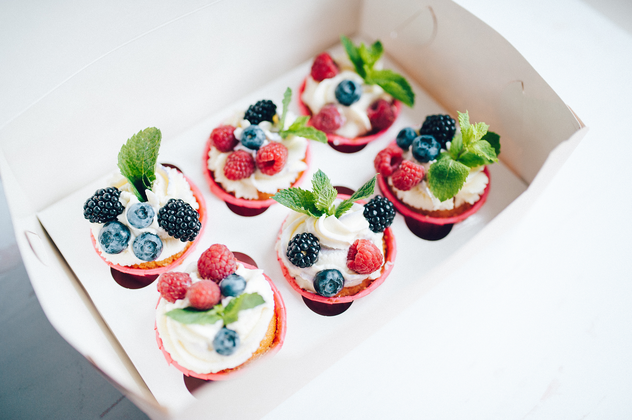 cupcakes decorated with cream, berries and miny in box.