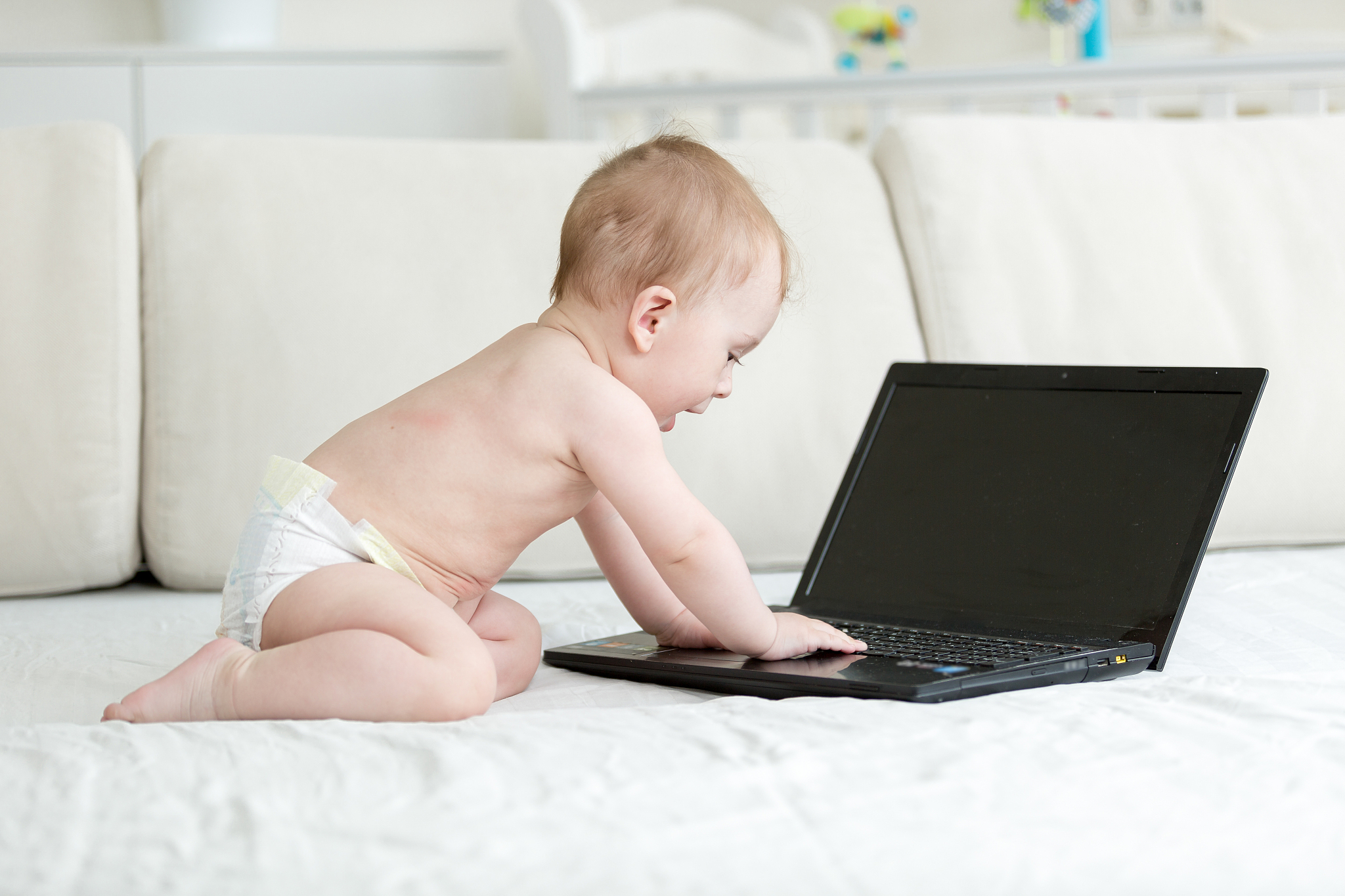 baby boy sitting on bed and using laptop