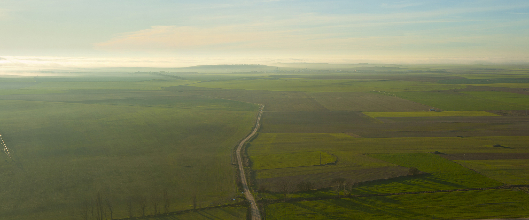 plowed and green fields in a valley with a path in the center an