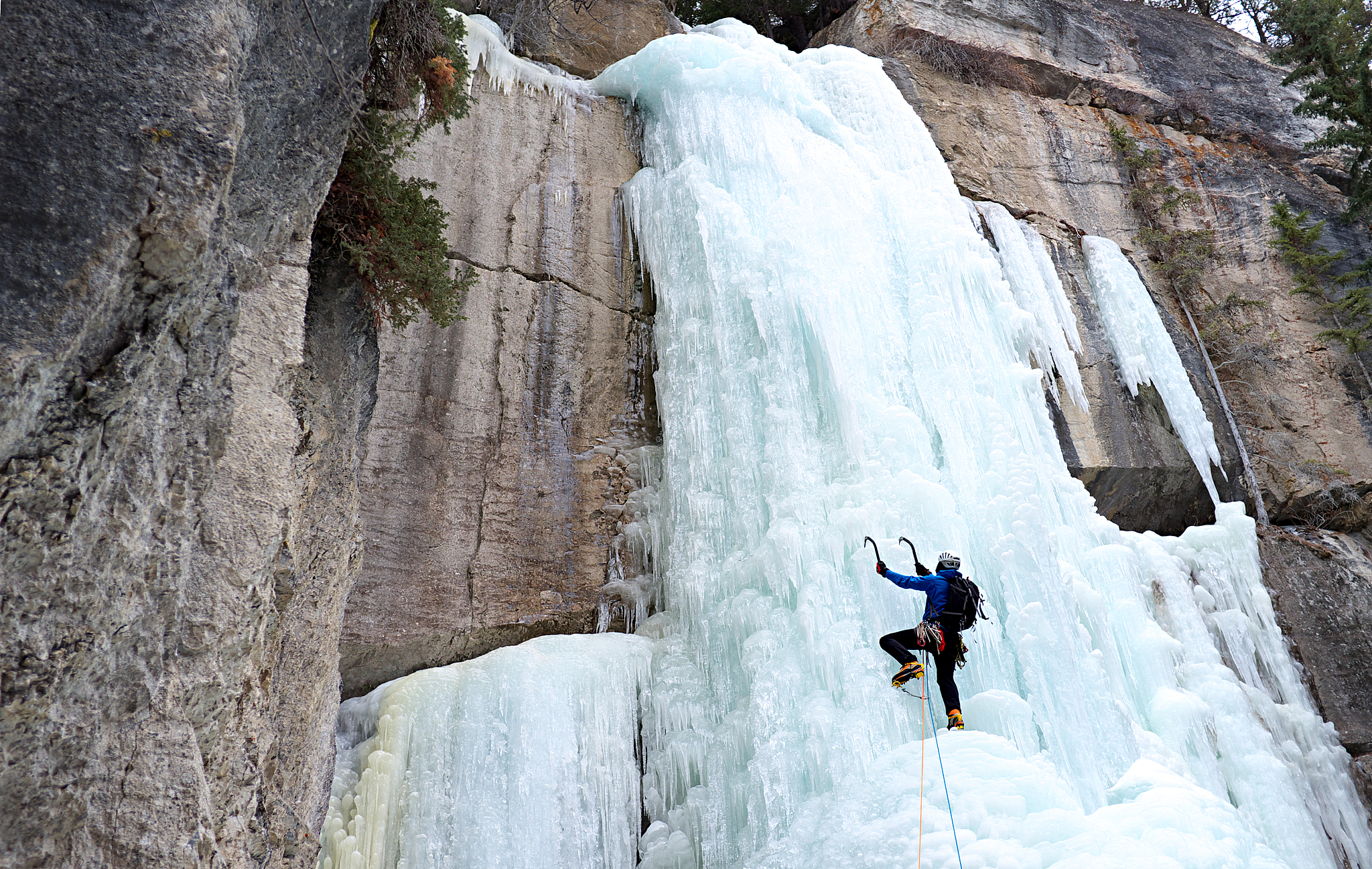 a man climbs frozen waterfall with ice axes