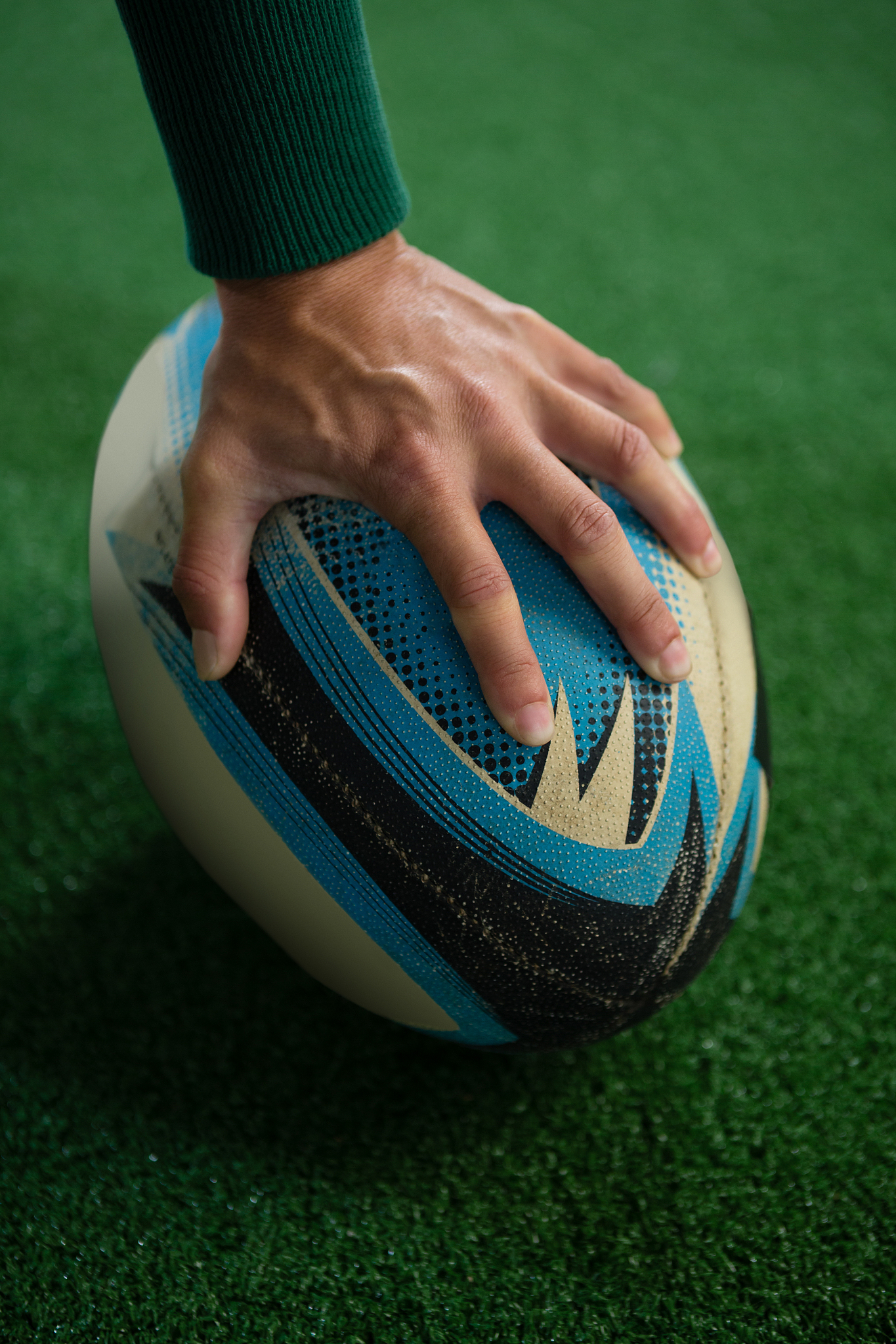 cropped image of hand holding rugby ball on playing field