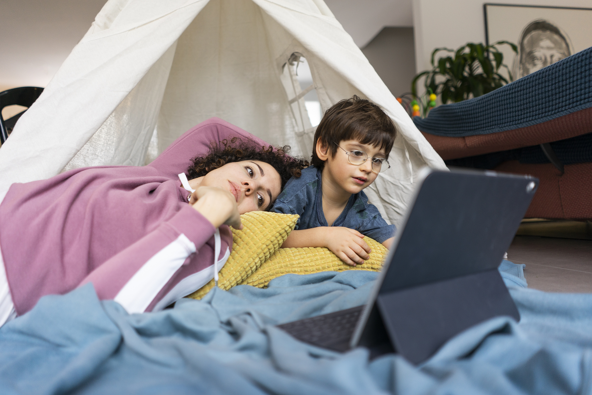 mother and son lying in play tent, watching movie on tablet