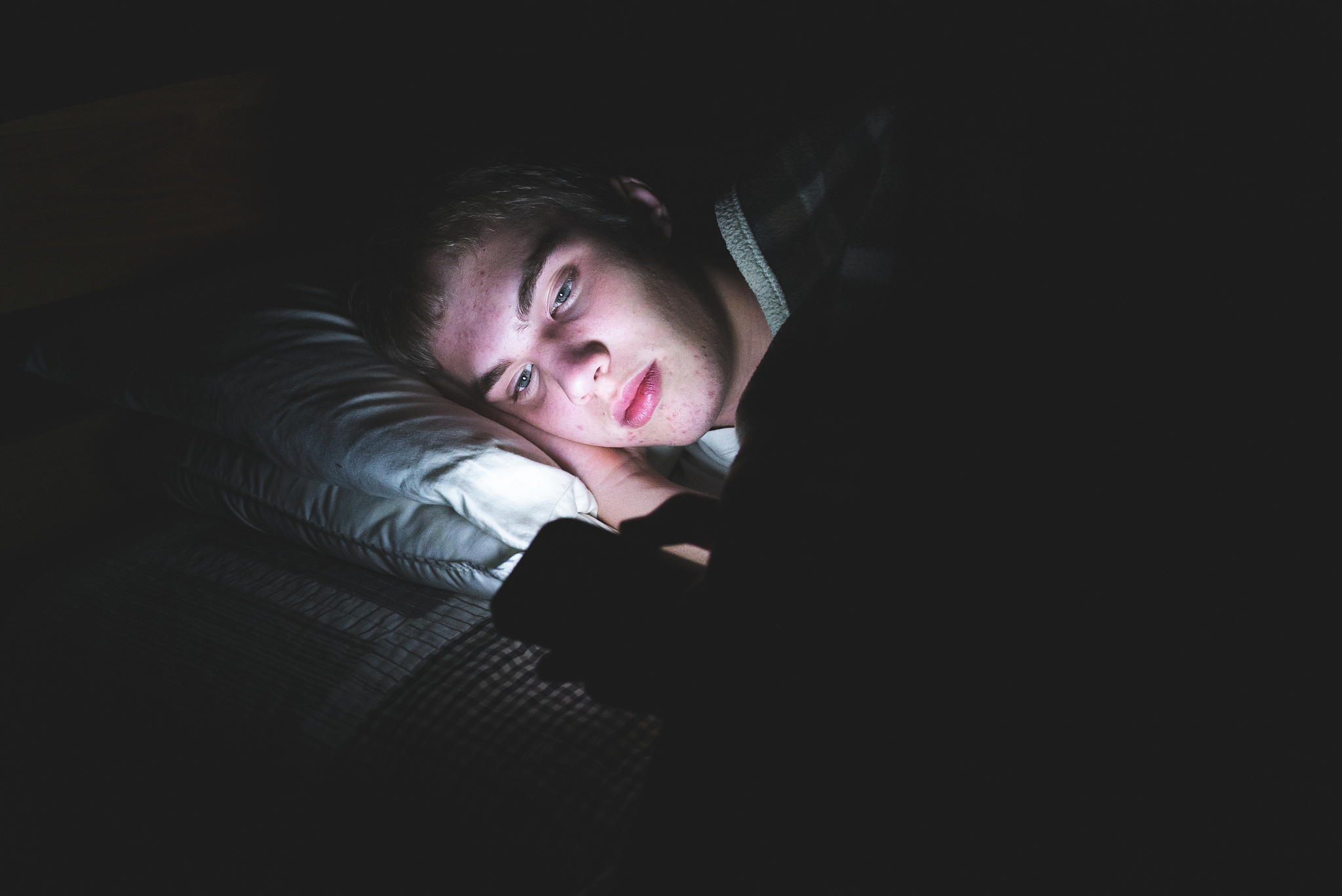 depressed teenager on his phone in the dark.