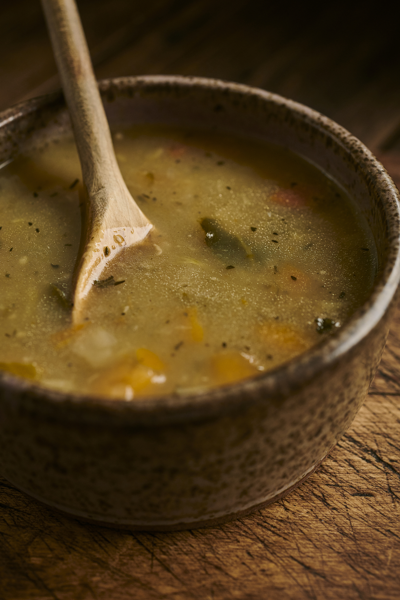 chicken and vegetable soup in a rustic bowl with wooden spoon.