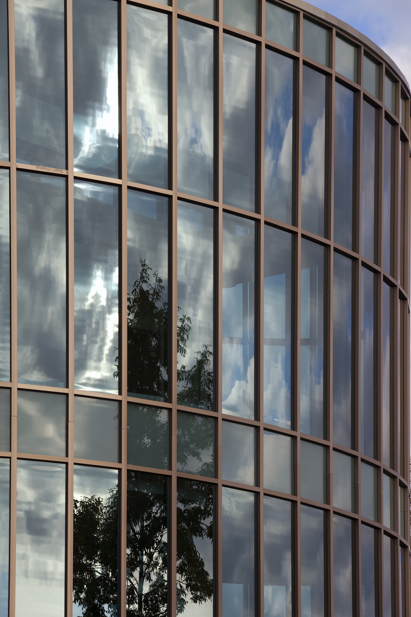 rounded glass walled building reflecting clouds