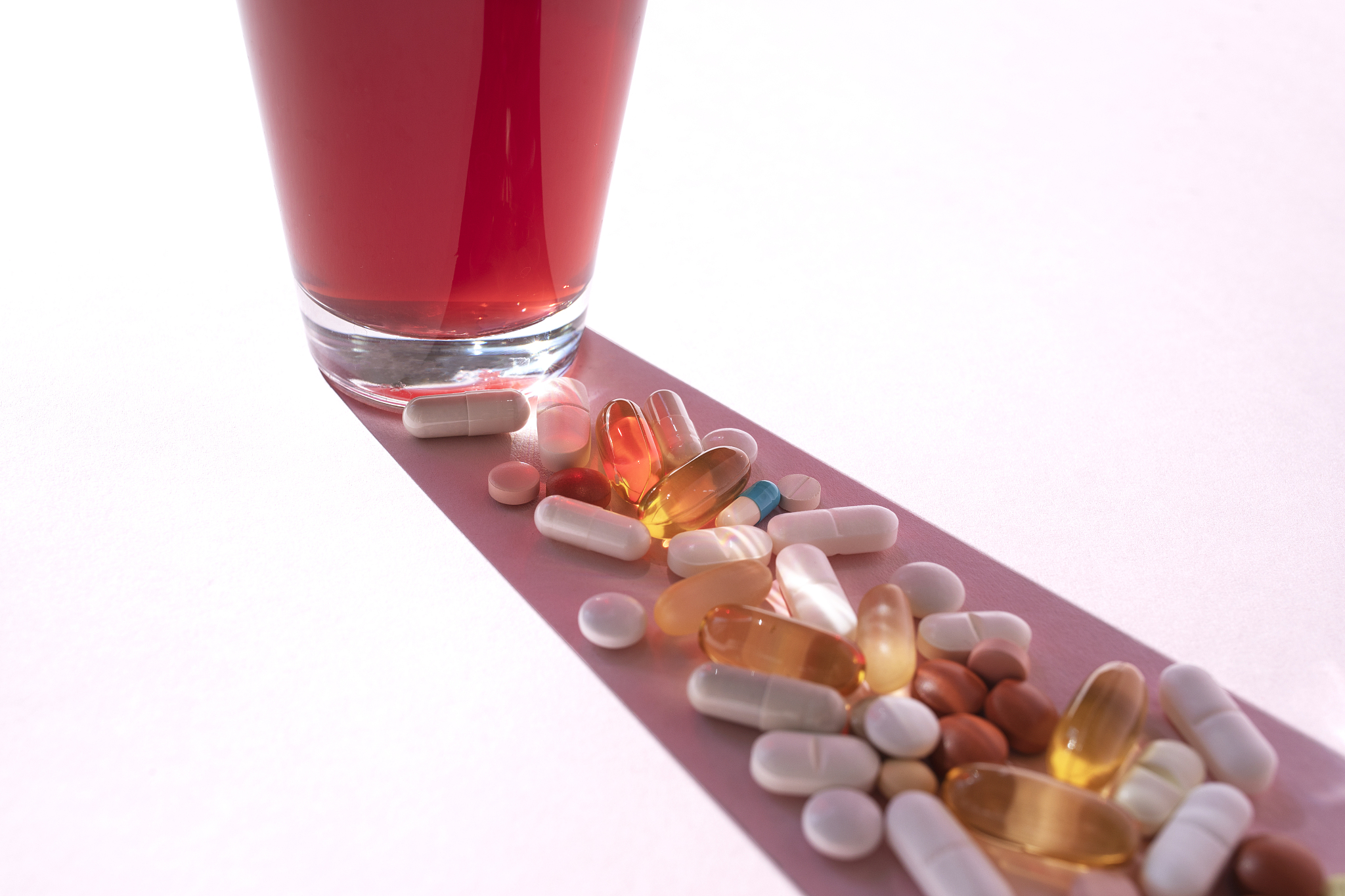 glass with various pills on the pink background