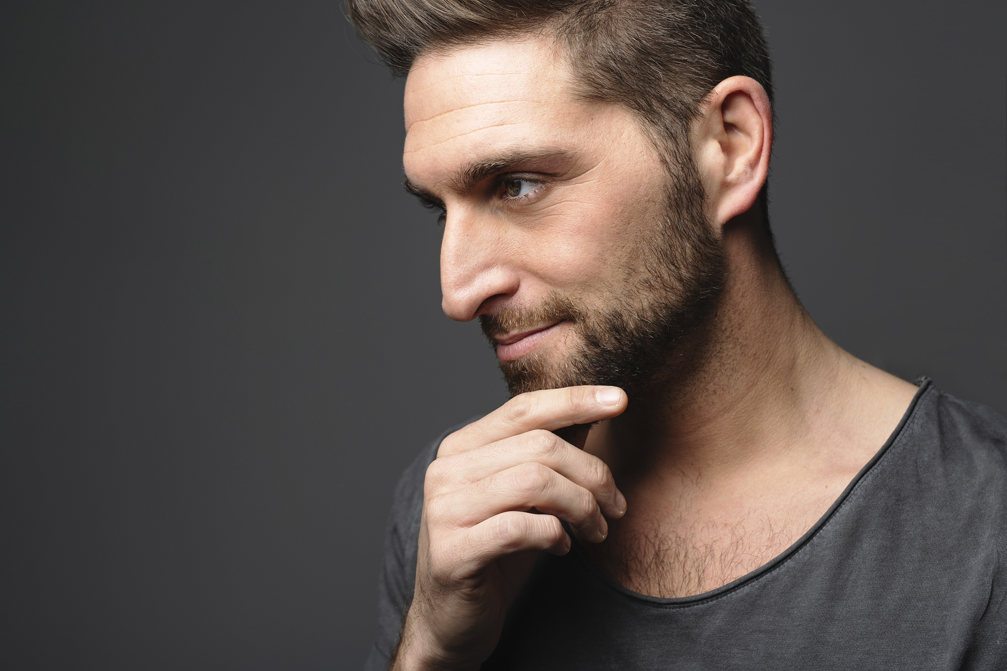 young man looking away while standing on dark background