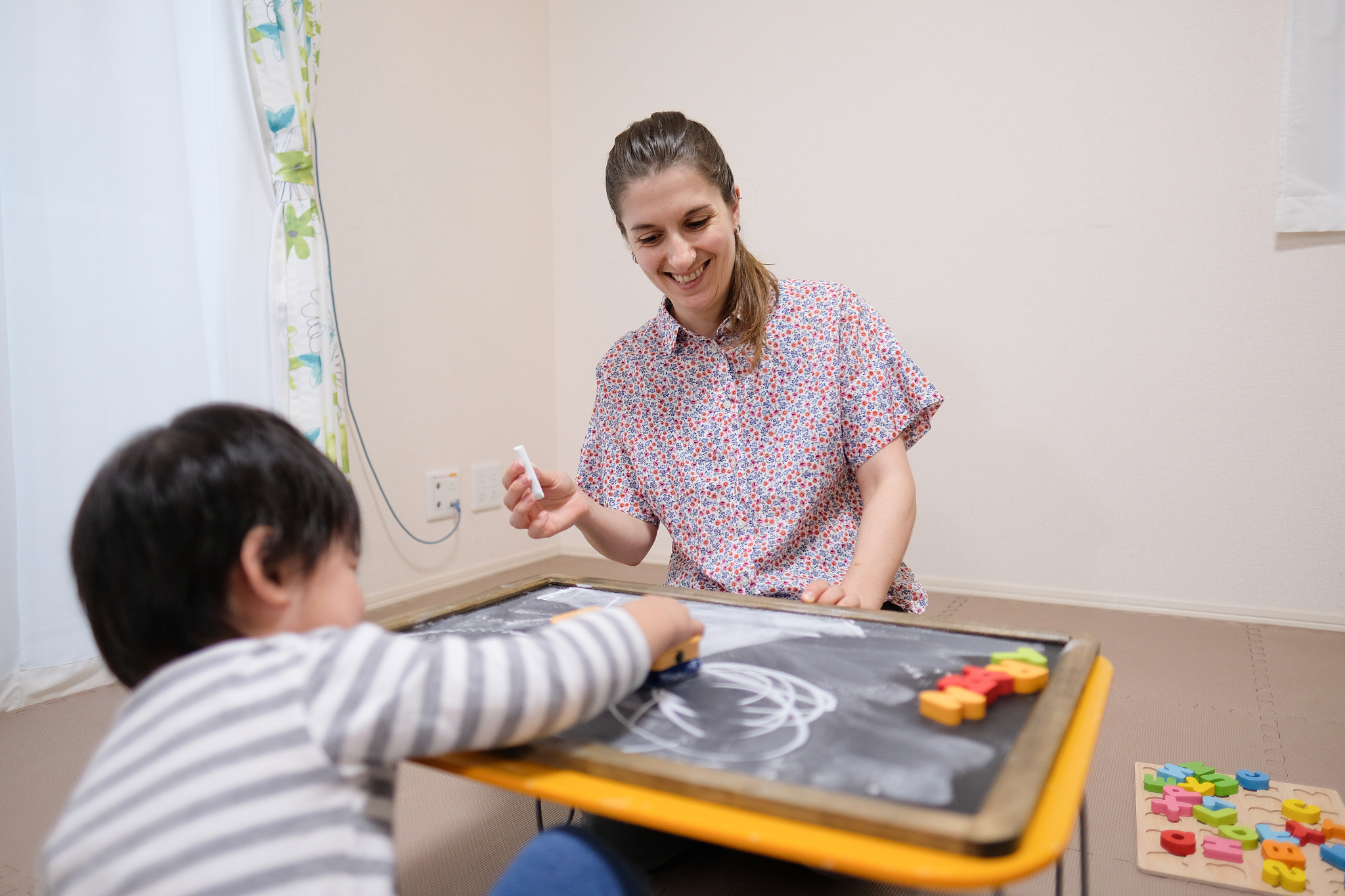 caucasian woman teaching toddler english with black board