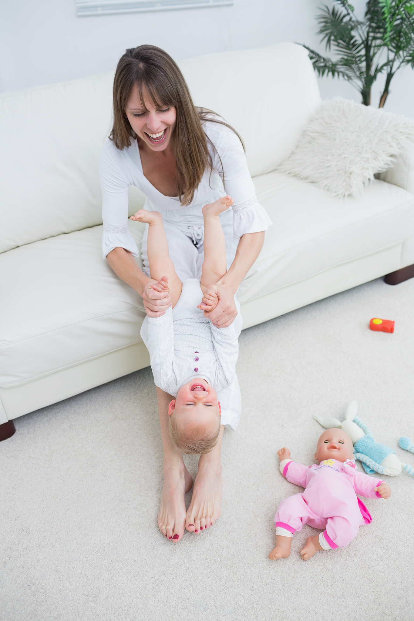 mother playing with a baby while sitting on a sofa in living roo