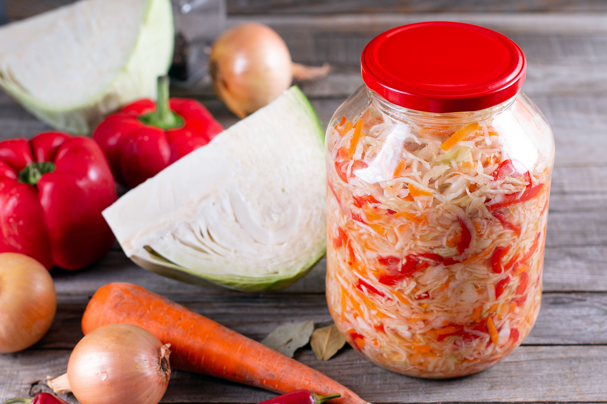 glass jar with homemade sauerkraut with ingredients on wooden ta