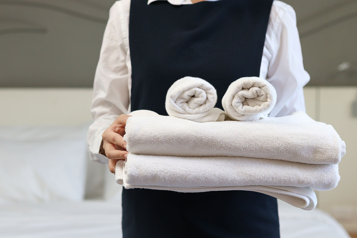 客房服务女佣清洁和整理床酒店房间概念,女客房服务员拿着一叠新鲜的