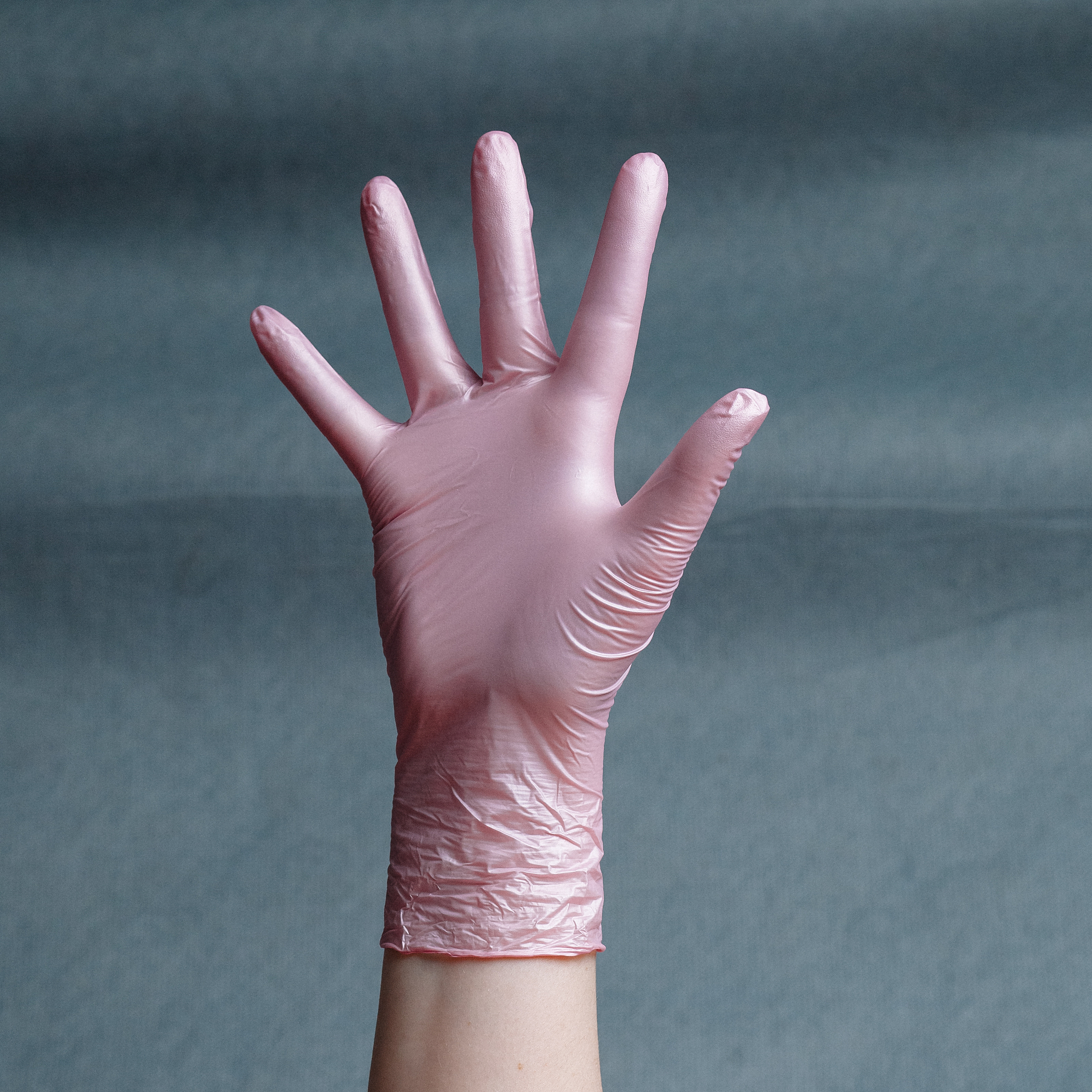hand in pink nitrile glove on a gray background with a gradient.