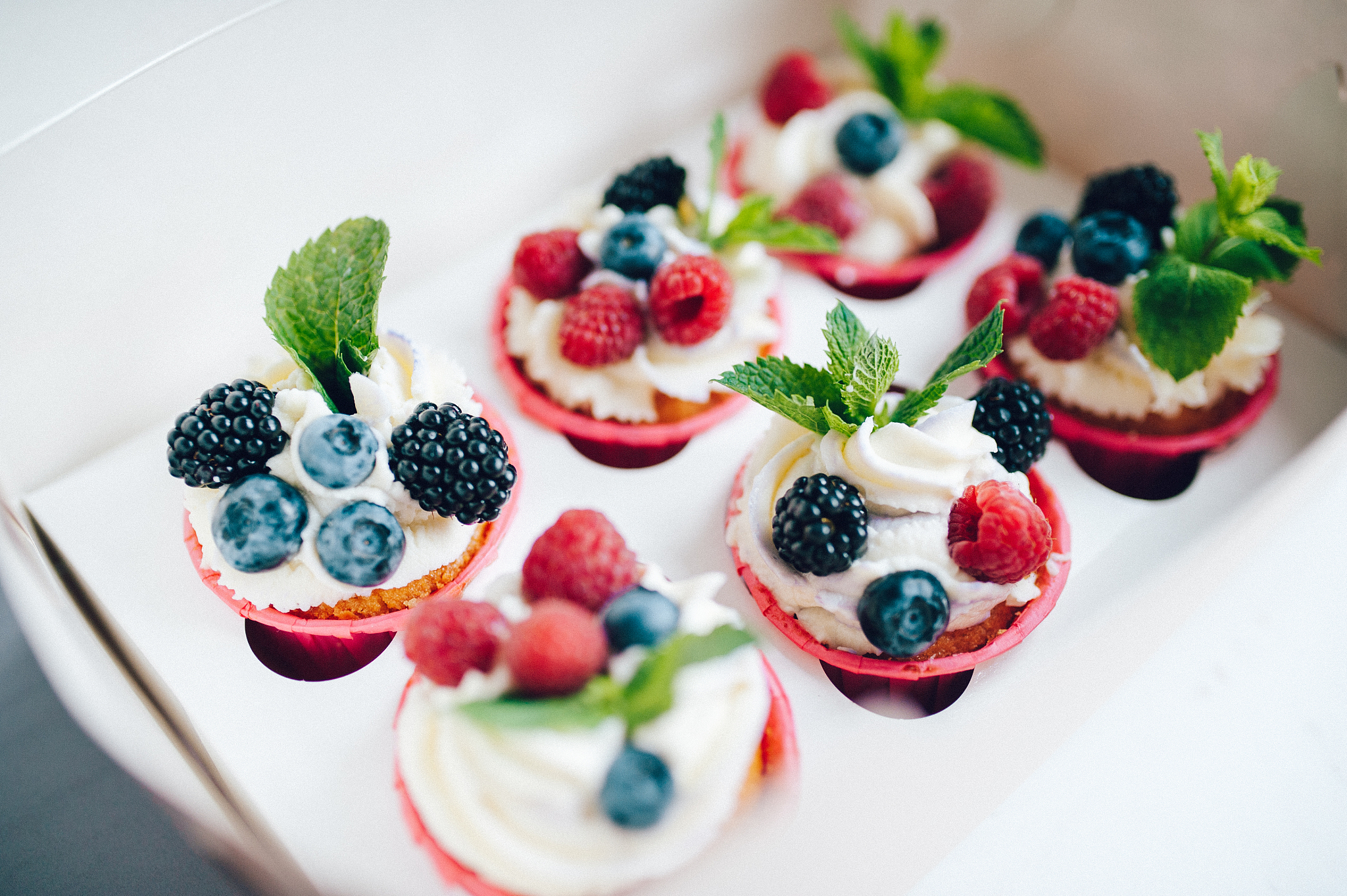 cupcakes decorated with cream, berries and miny in box.