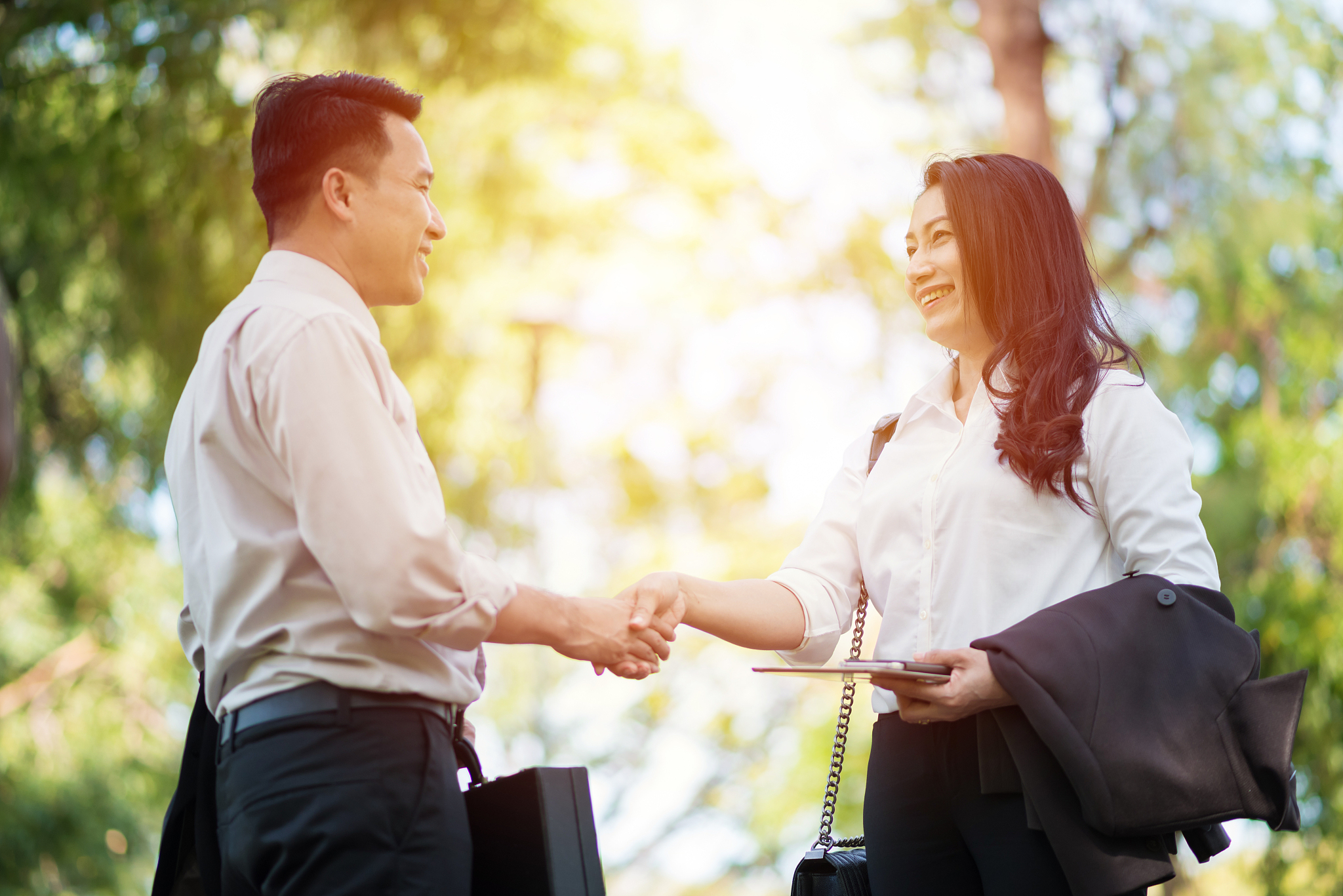 businessman shaking hand with colleague against trees at park