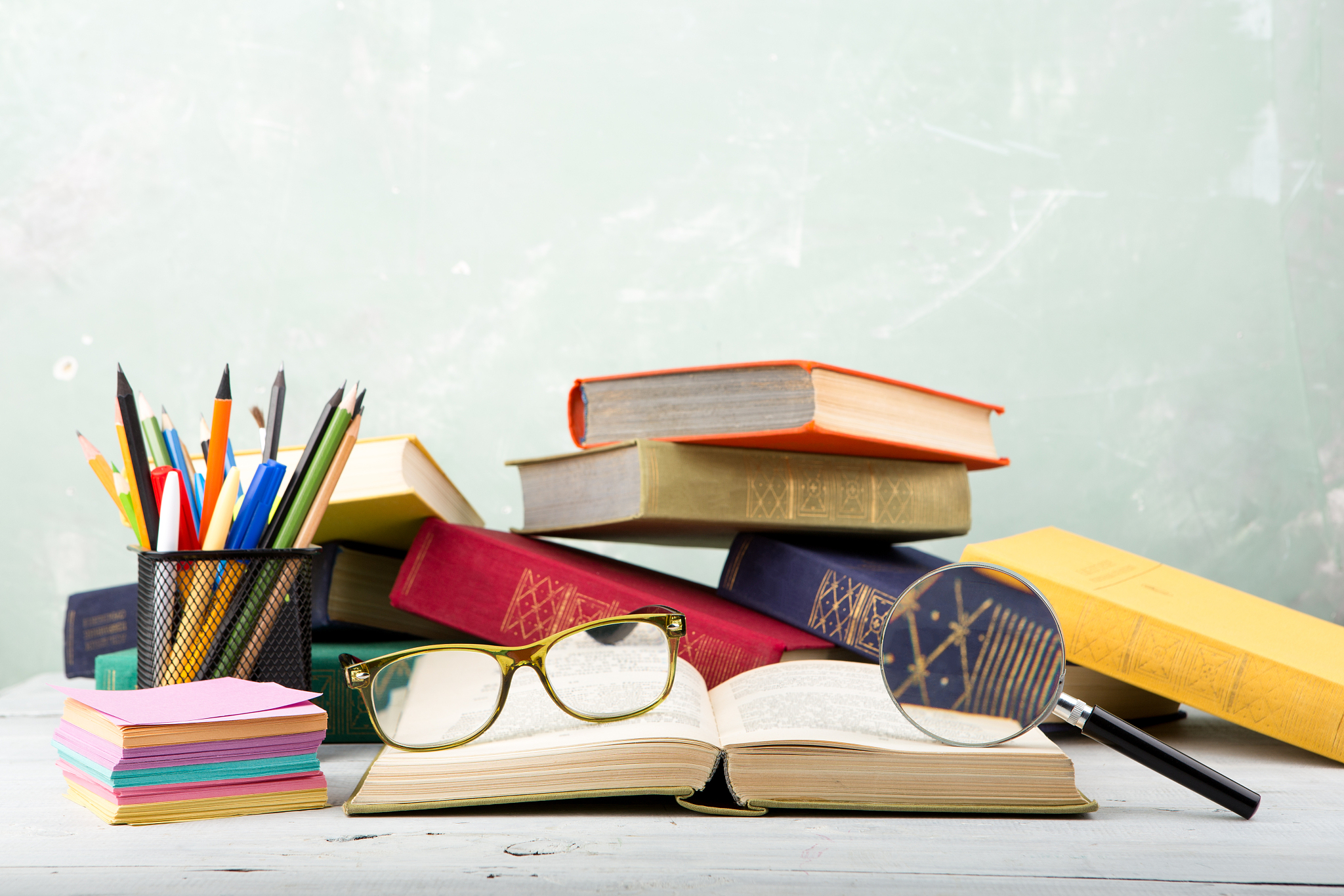 a stack of books, glasses, stationery and magnifying glass