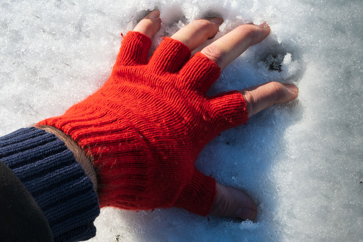 男人的手指带着红色的手套在雪地上做雪球