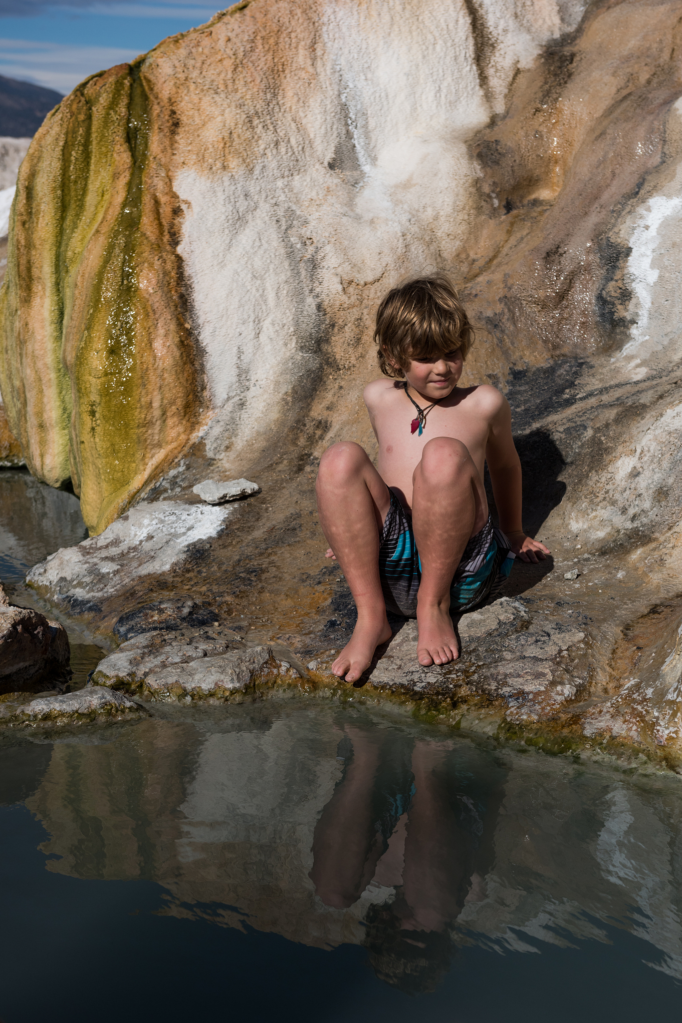 child sit at the edge of a beautiful natural hot springs in the 