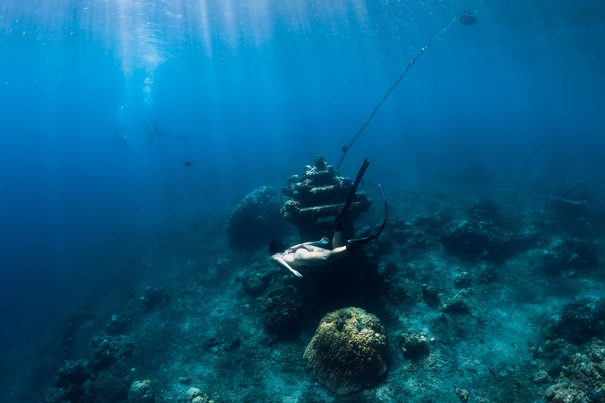 young woman free diver glides with fins near underwater temple. 
