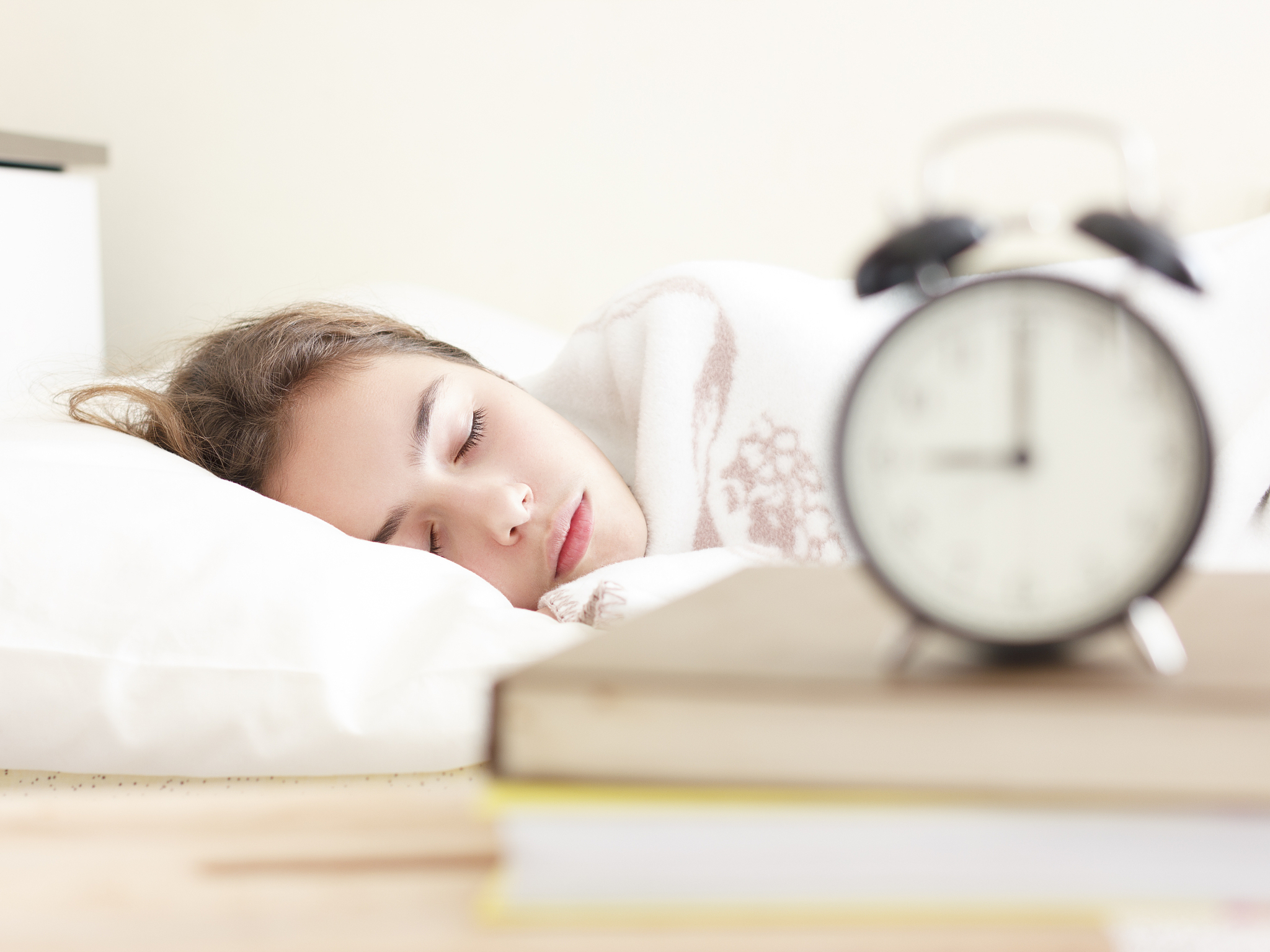 teenager girl sleeping in a white bed. alarm clock in the foregr