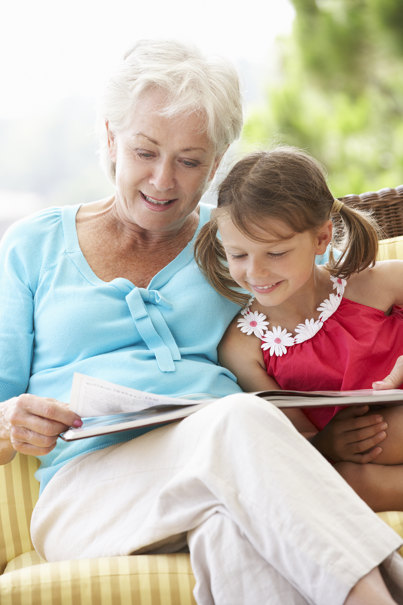 grandmother and granddaughter reading book on garden seat