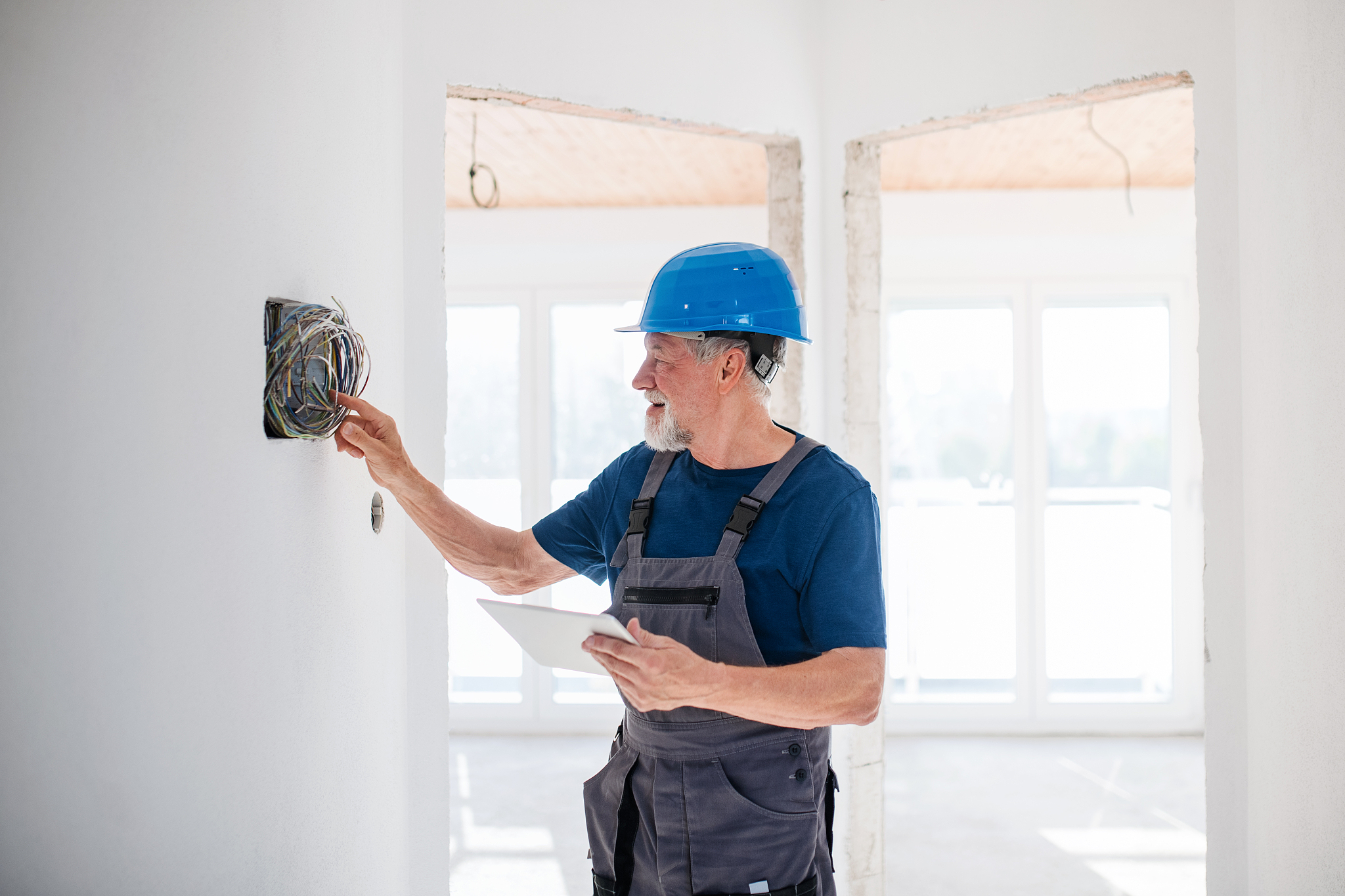 senior man electrician with helmet working indoors on house cons