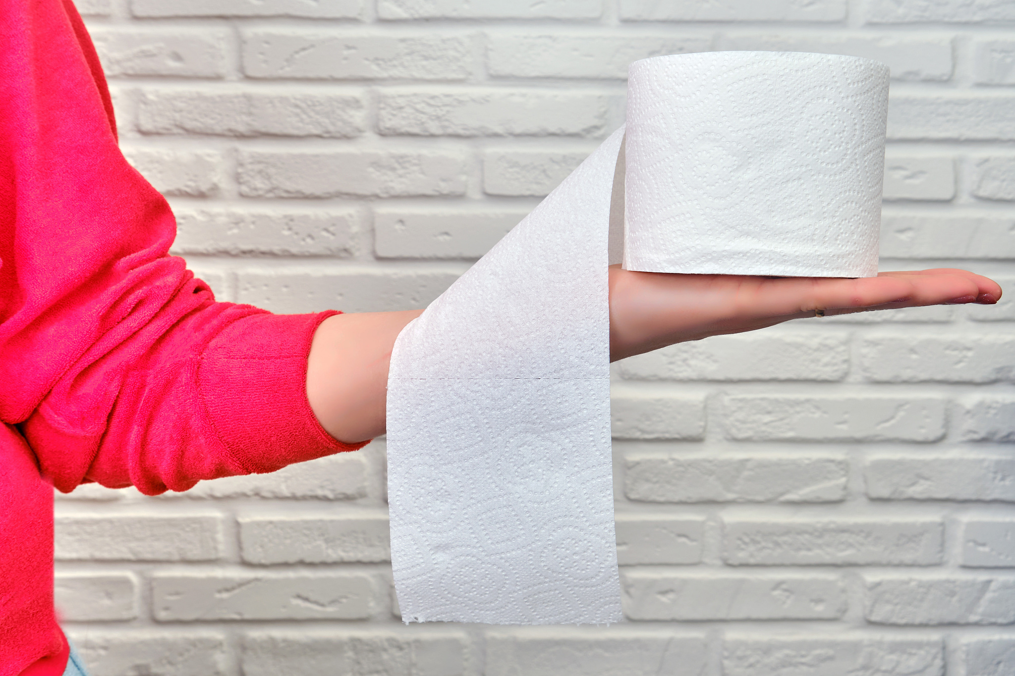 a young woman holds toilet paper in her hand, white brickwall ba