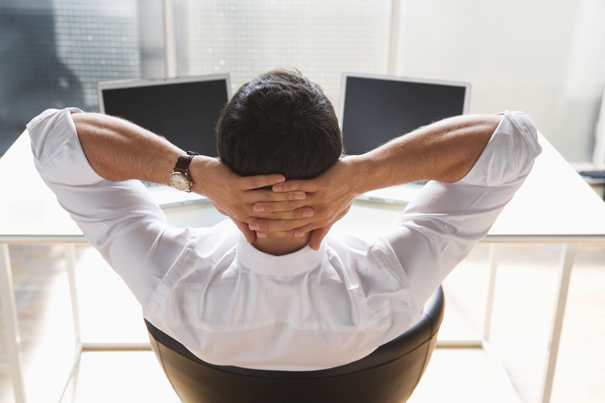 business man relaxing, two laptops on desk, back view