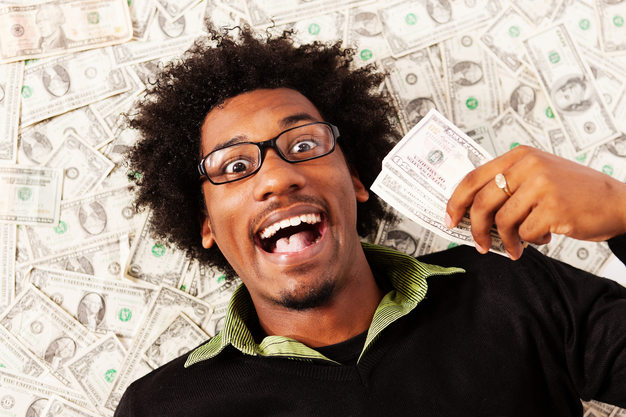 rolling in money! young man with multiple dollars is triumphant
