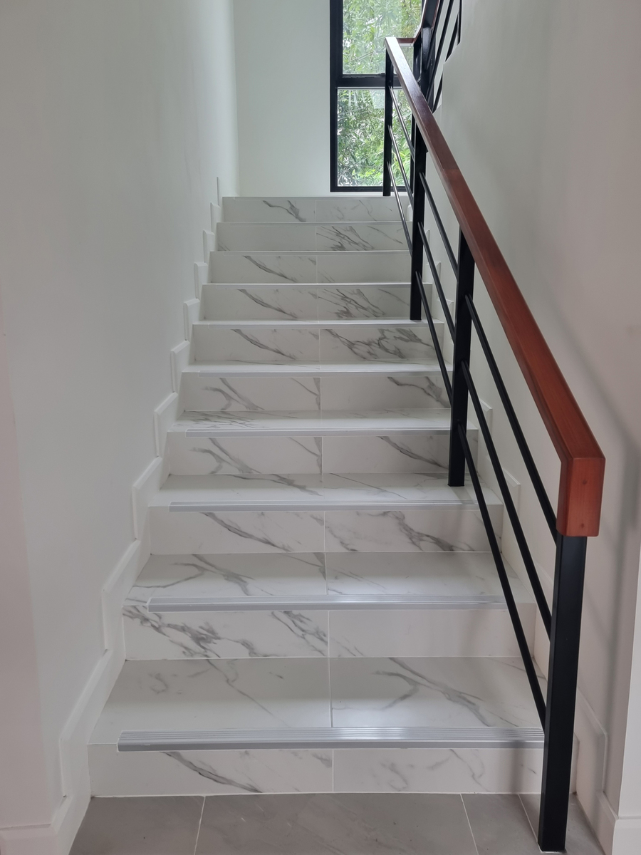 用一段话描写：大厅两侧矗立着两条优雅的L型楼梯上面铺上了精致的红地毯用于通往二楼连廊。