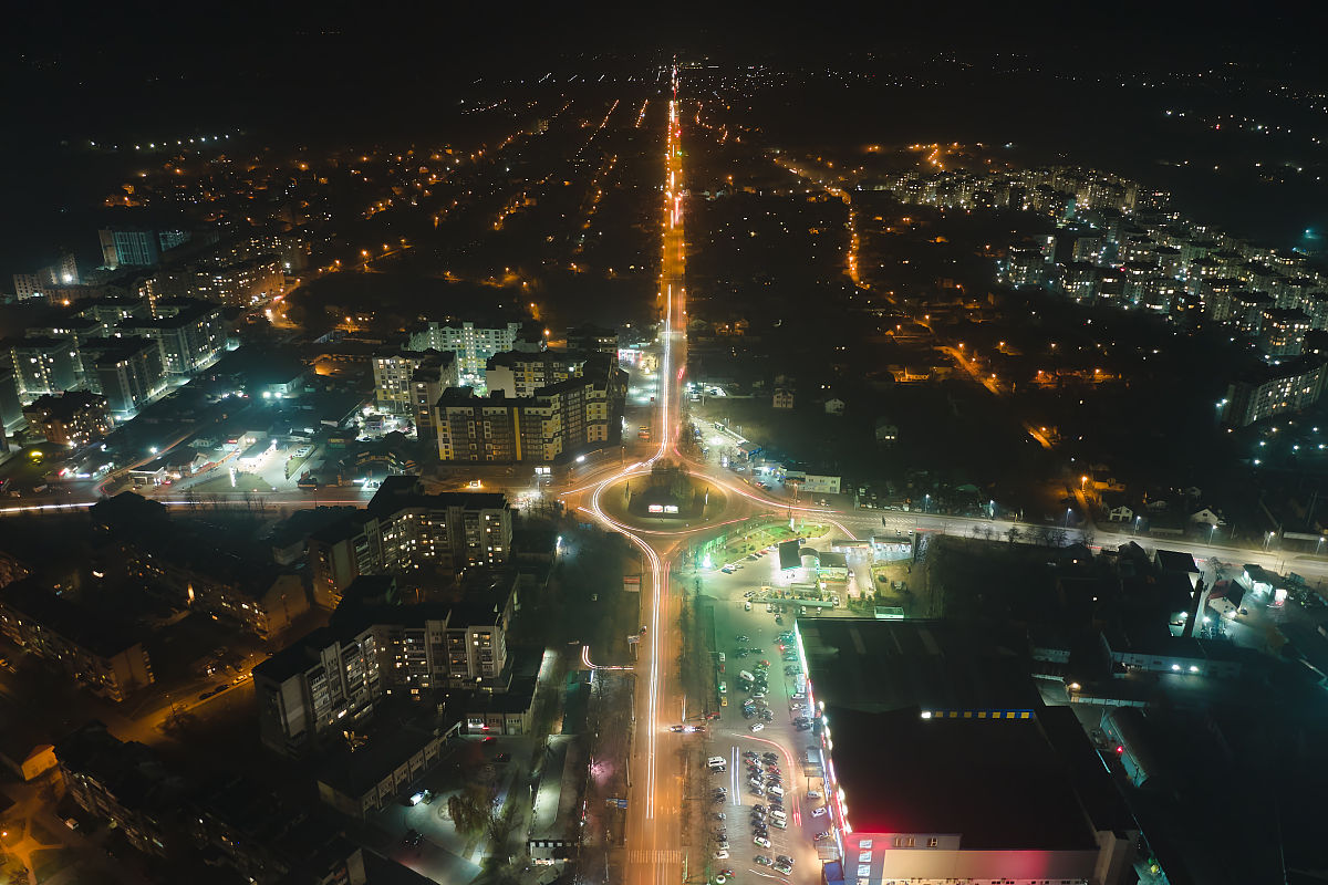 夜间城市住宅区街道上的高层公寓和灯光明亮的环形交叉路口鸟瞰图.黑
