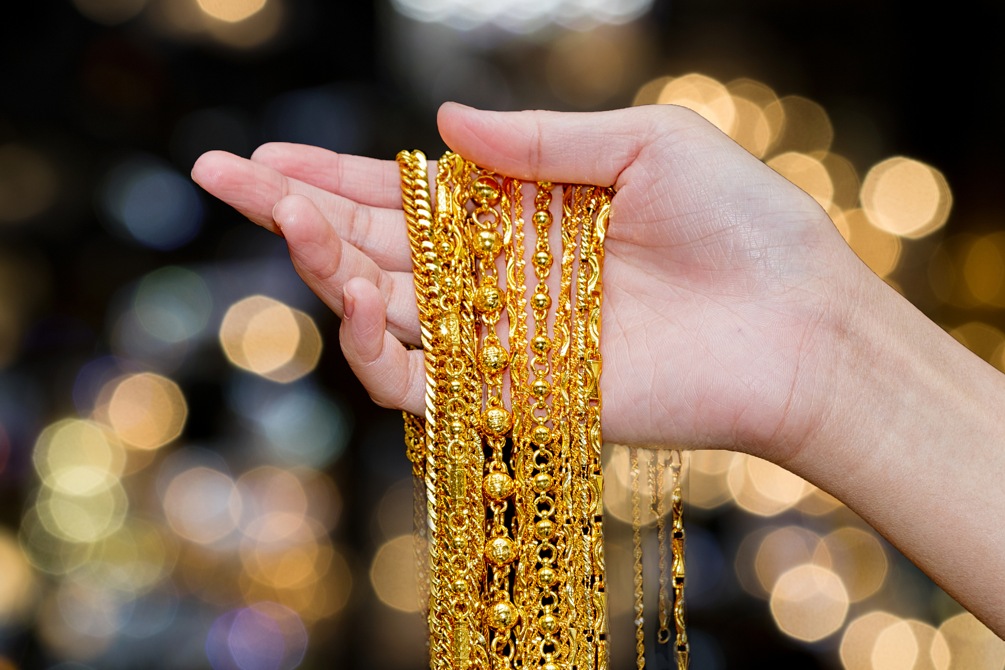 cropped hands of woman holding bracelet against illuminated ligh