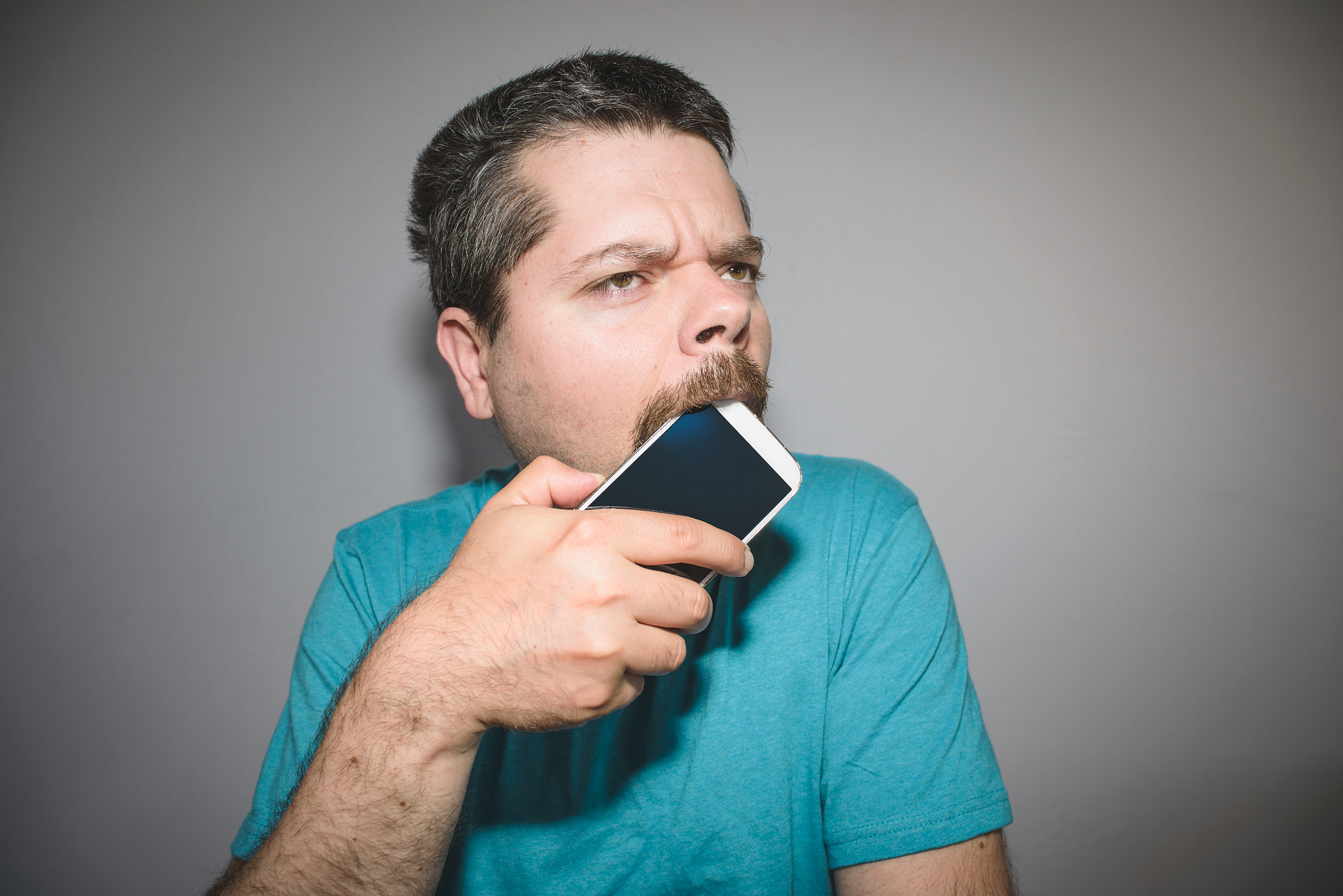 man biting and chewing on his smart phone