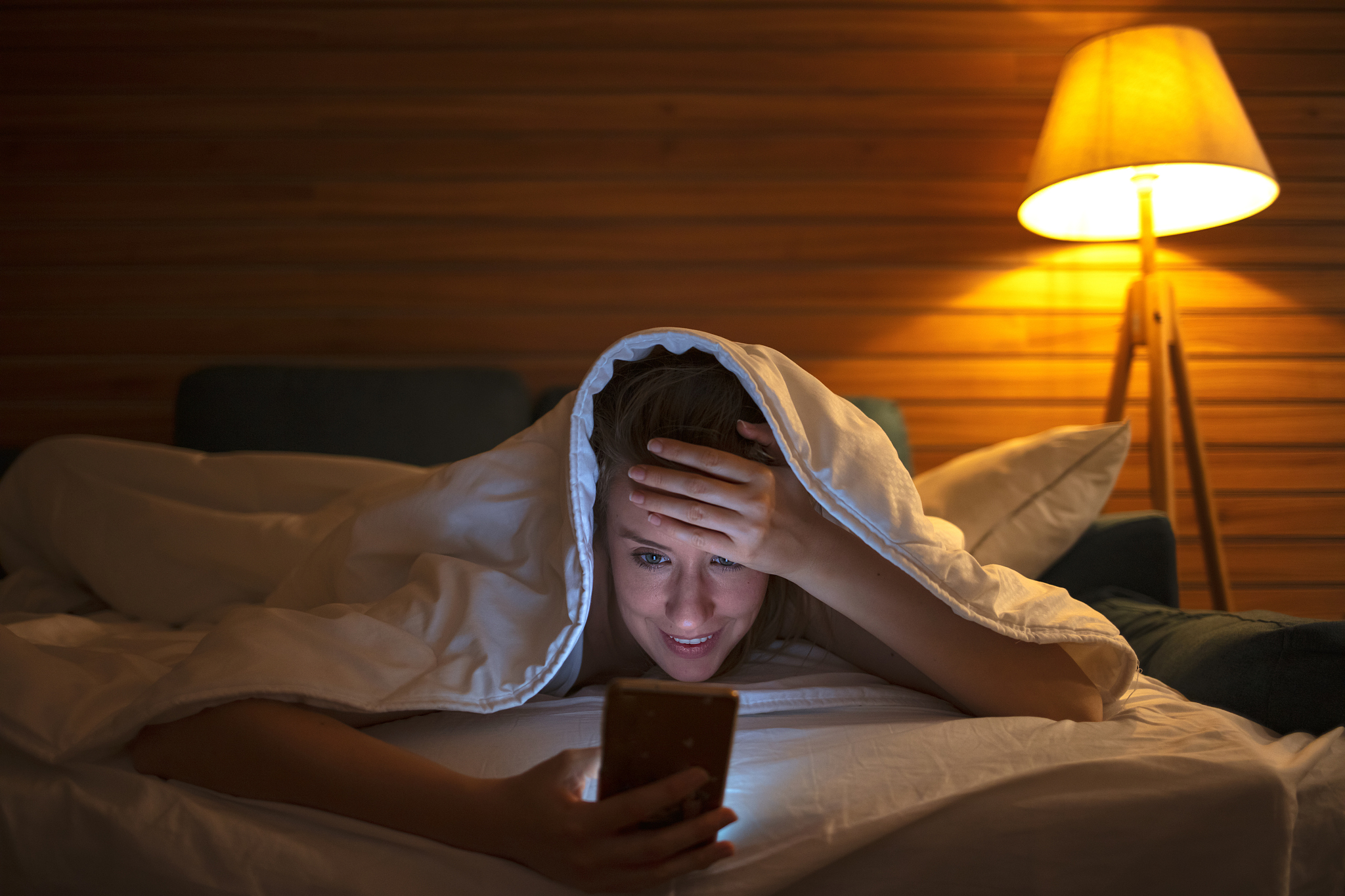 woman using her phone under blanket in bed at night.