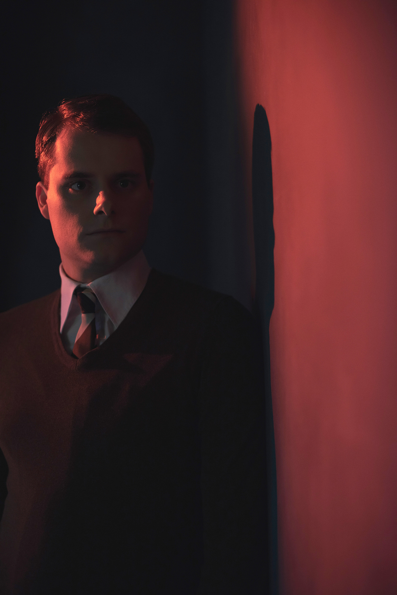 man in white shirt and brown sweater in red light.