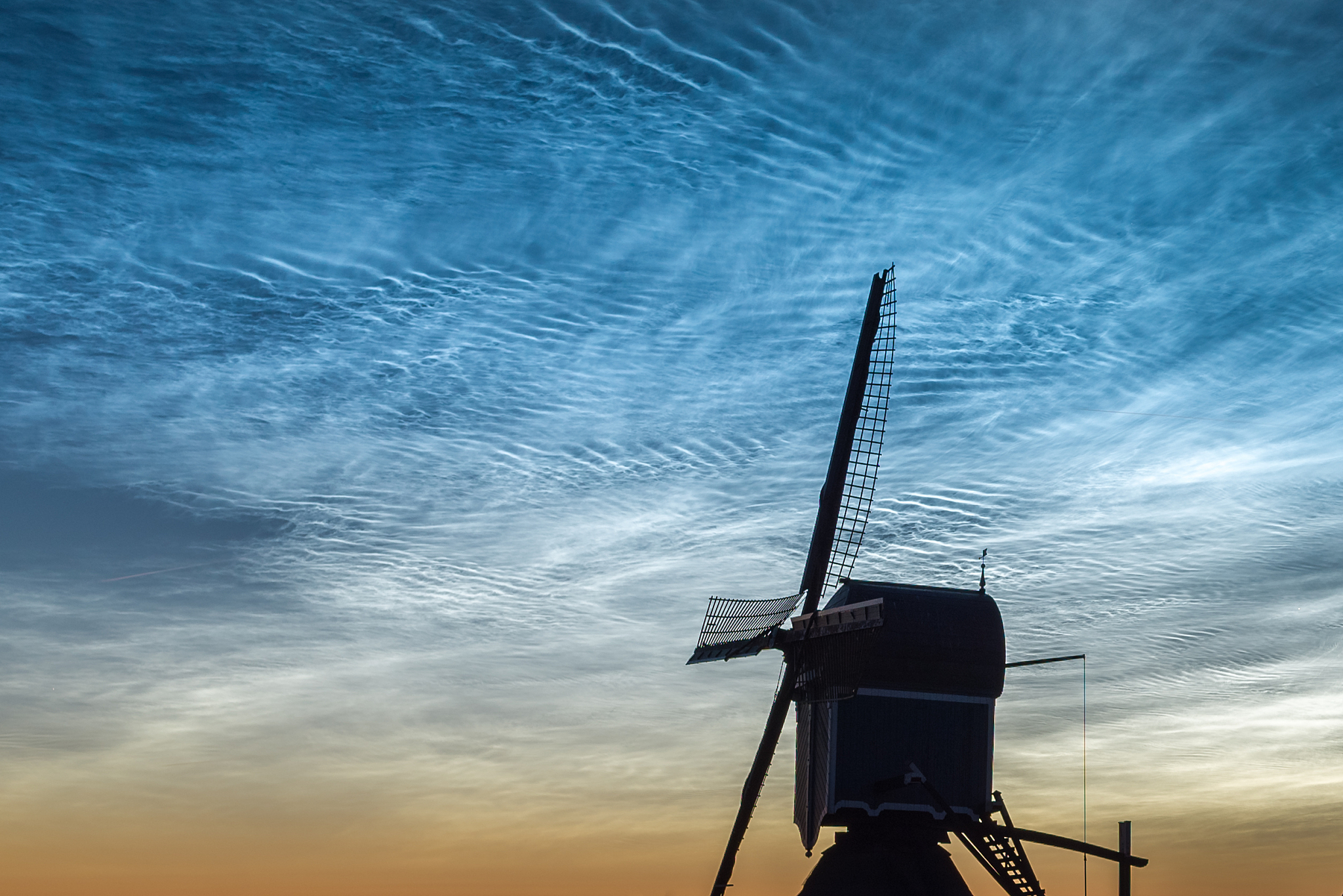 windmill is silhouetted against a sky full of noctilucent clouds