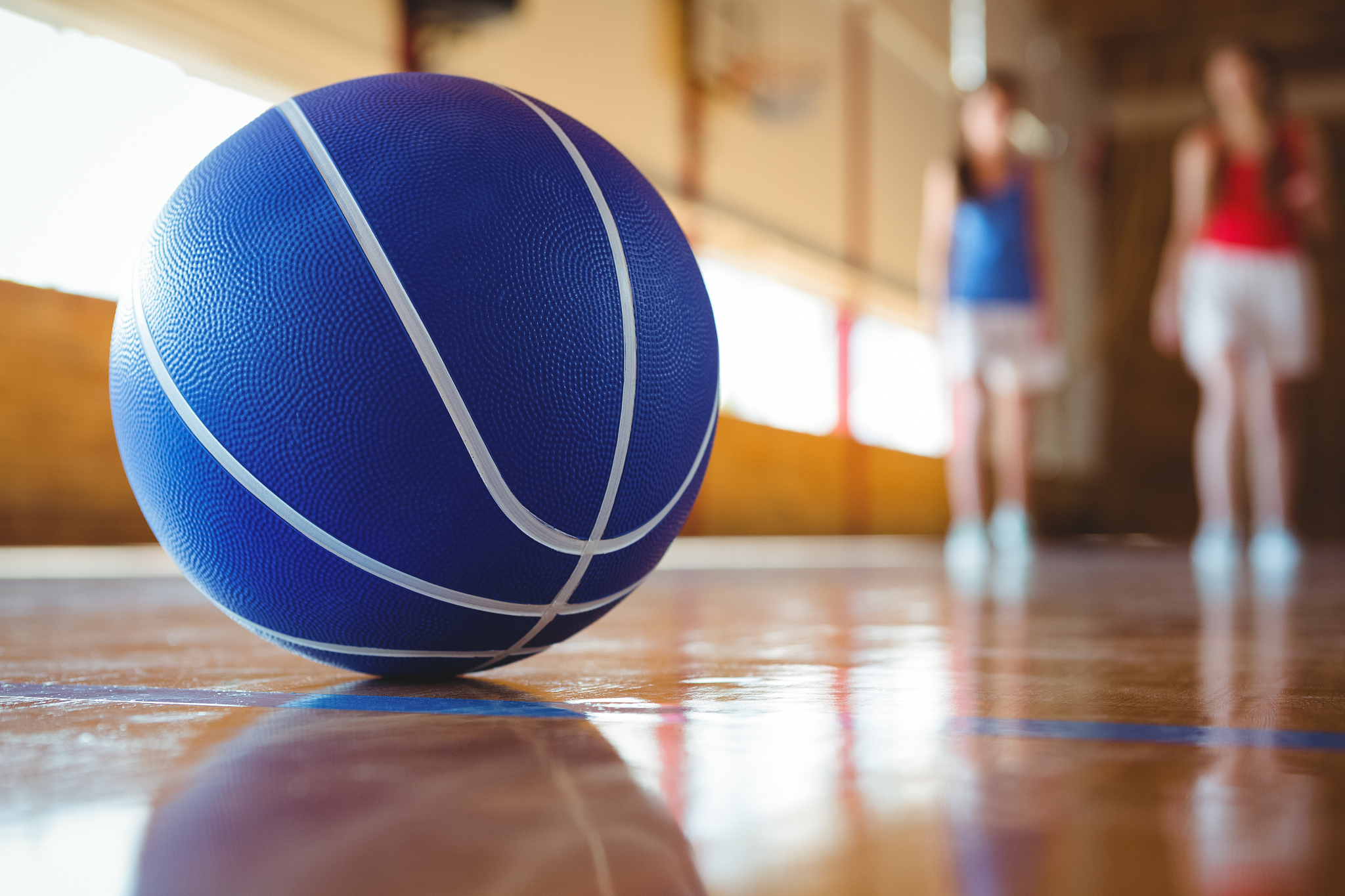 close up of blue basketball on floor with female players in back