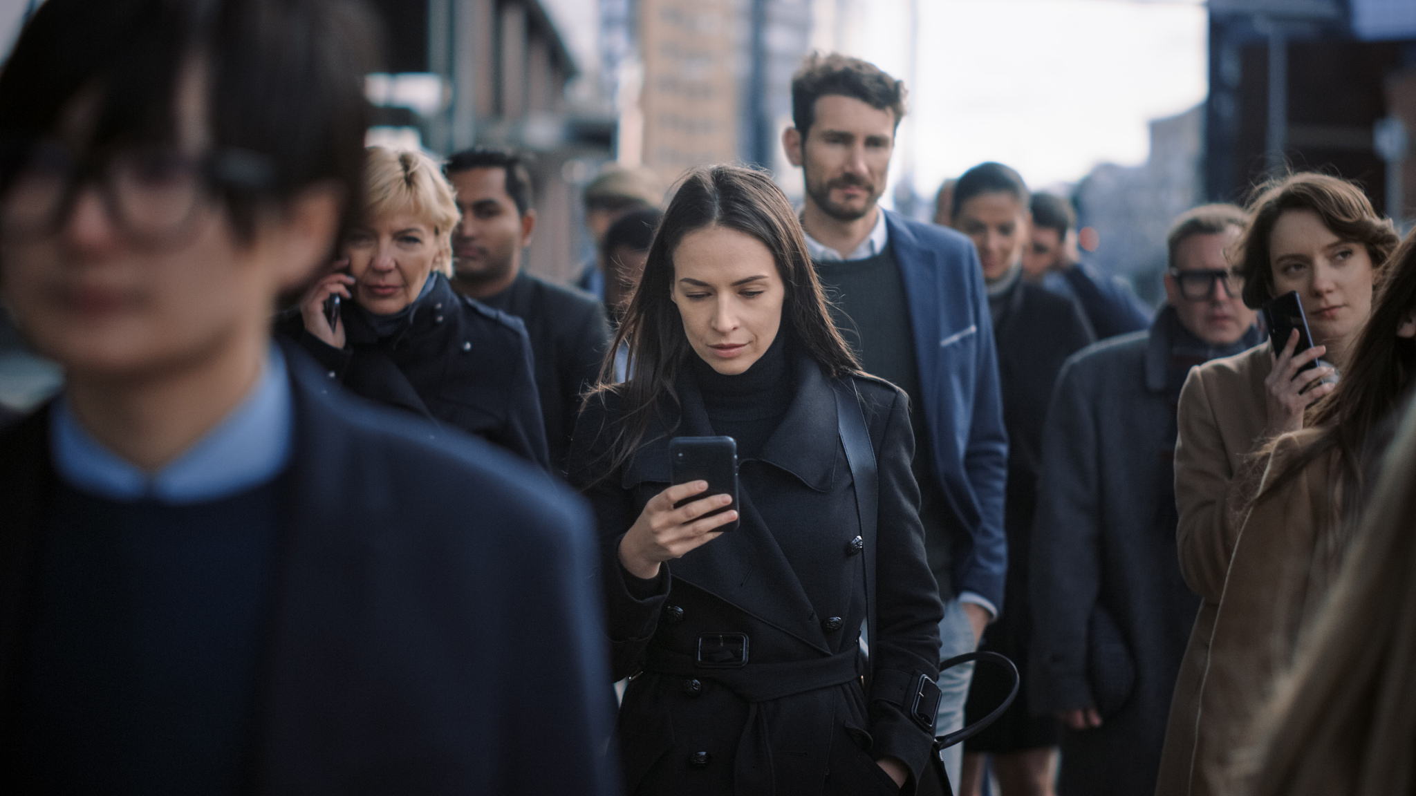 beautiful businesswoman in black coat is using a smartphone on a