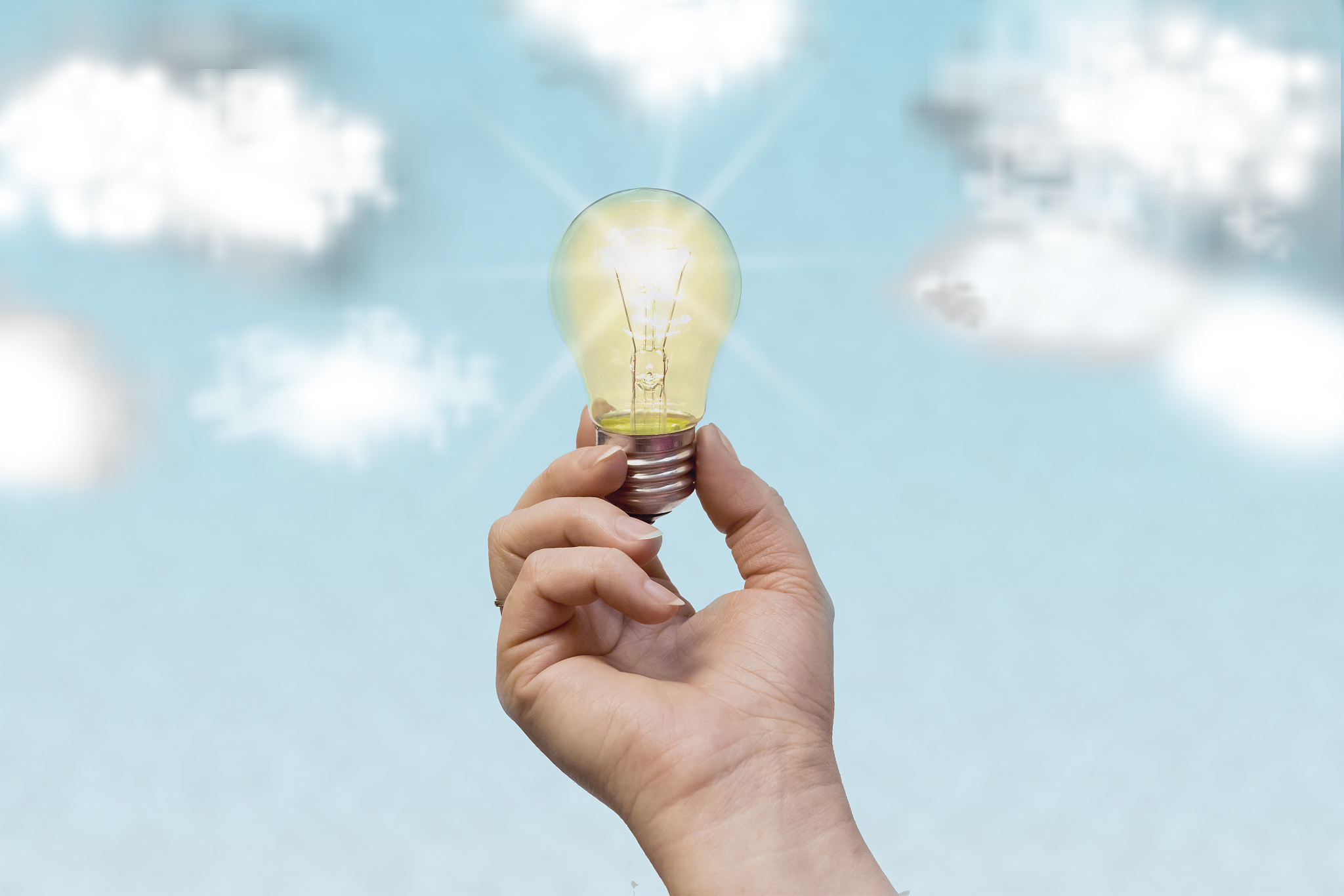 the man's hand holds a glowing lamp against the blue sky.