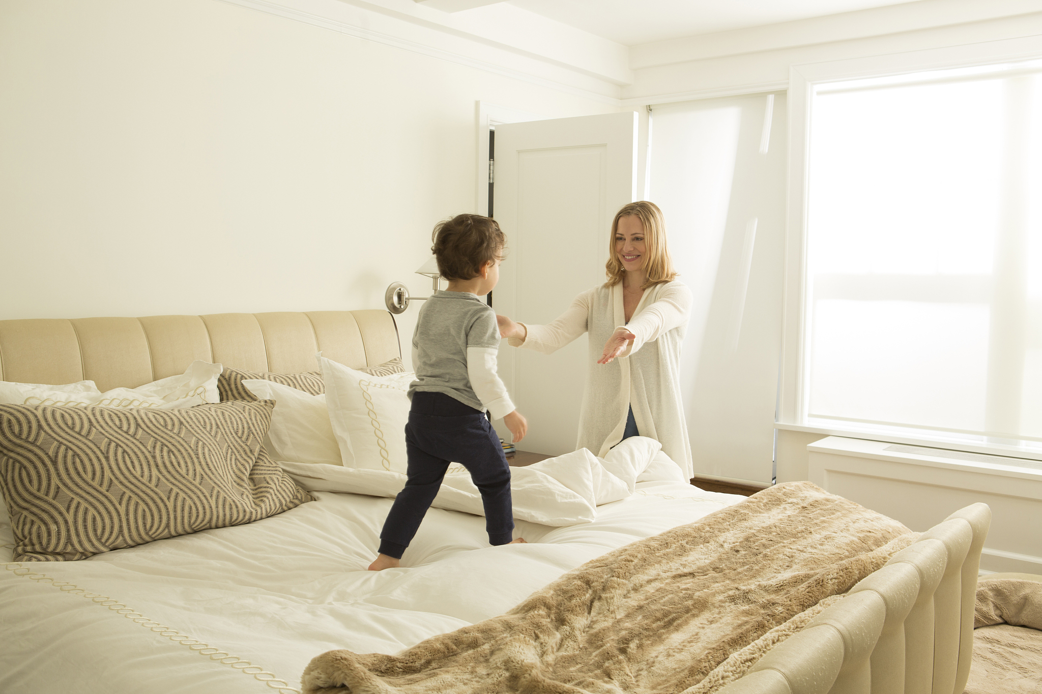 woman opening arms to toddler son on bed