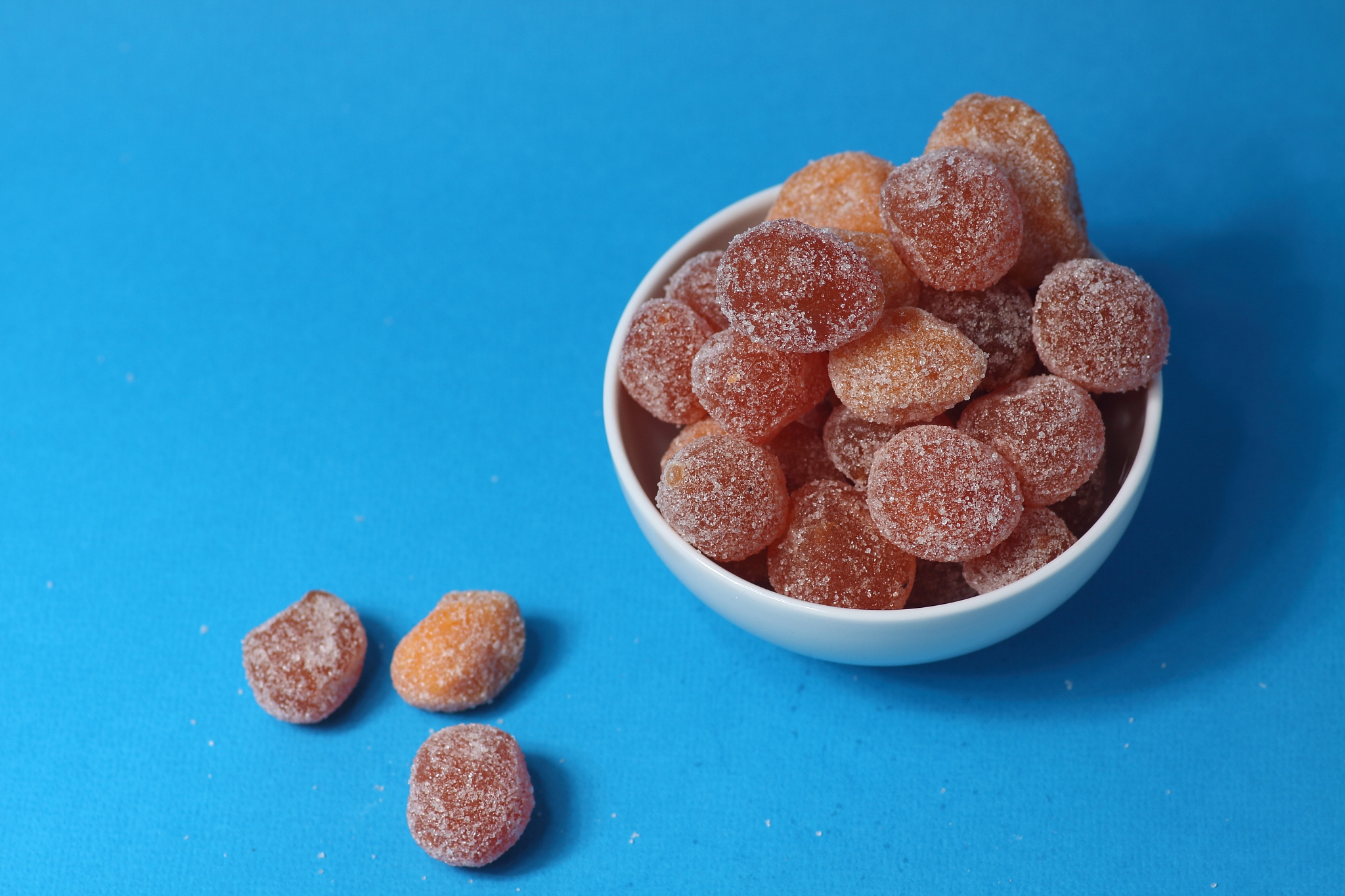 a bowl of kumquat coated with sugar isolated on blue background 