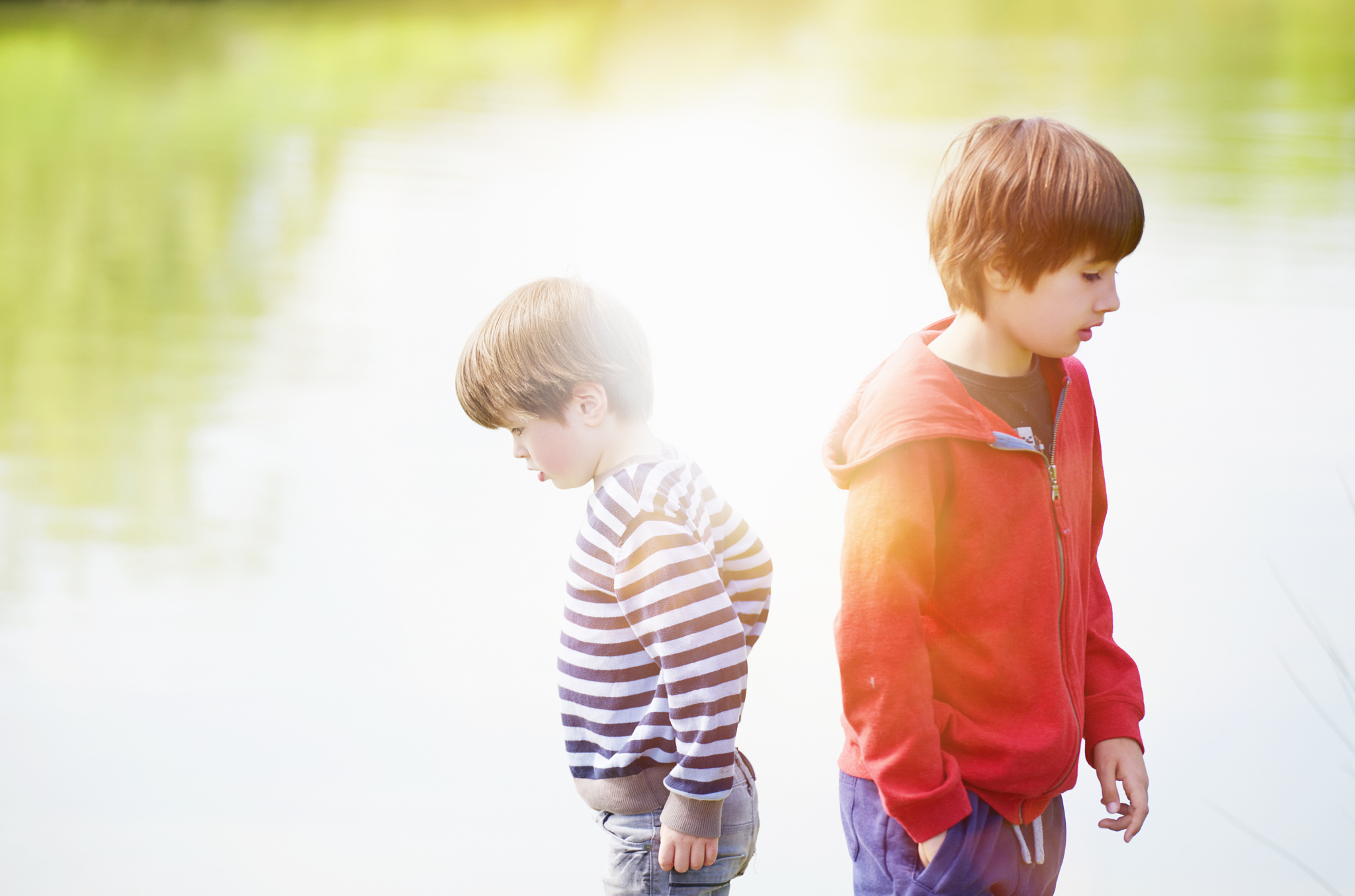 two boys standing by a lake with tree reflection