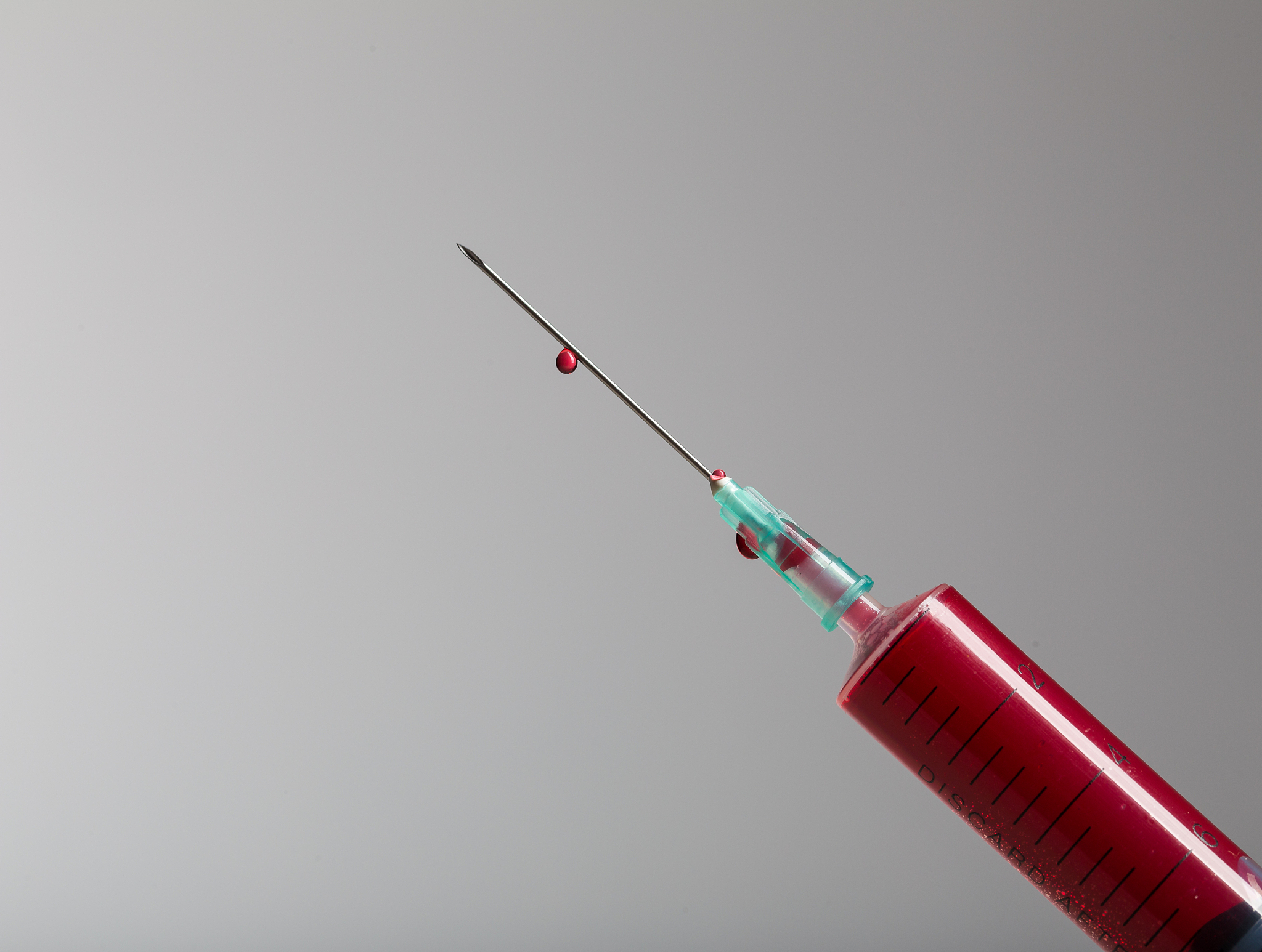 close up of a single drop of blood hanging at the end of a needl