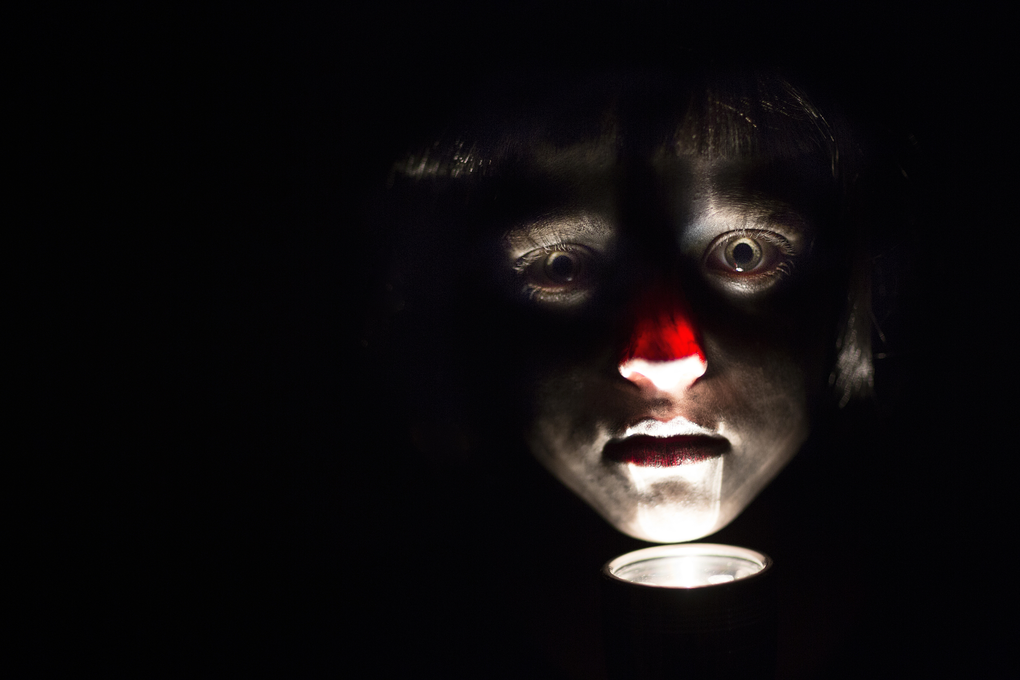 spooky, staring girl with face painted like a zombie and lit by 